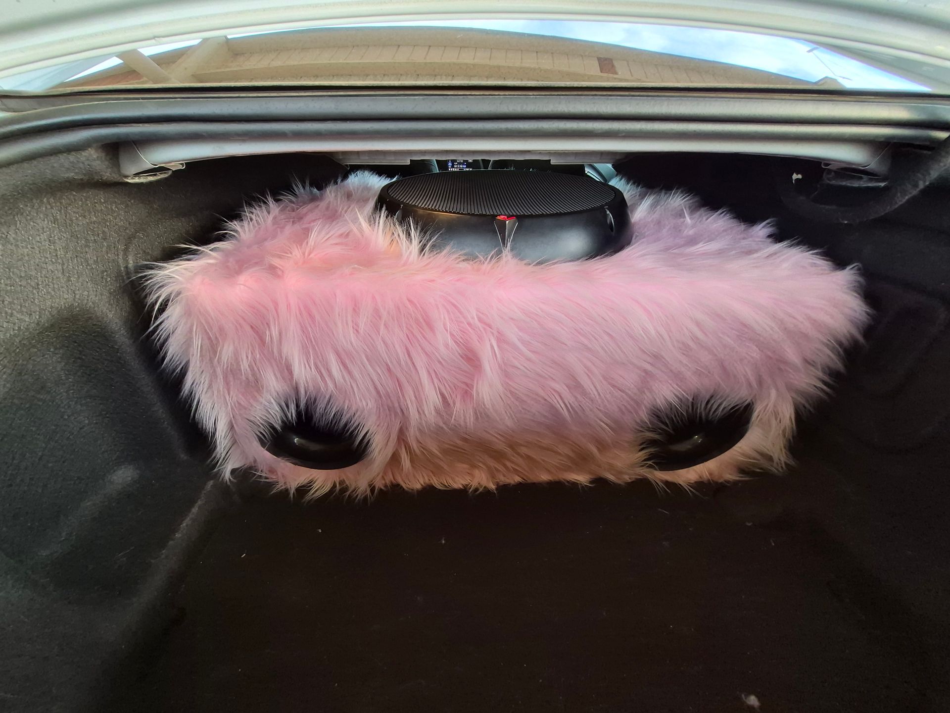 Pink fuzzy car trunk organizer with black mesh pockets inside a vehicle trunk
