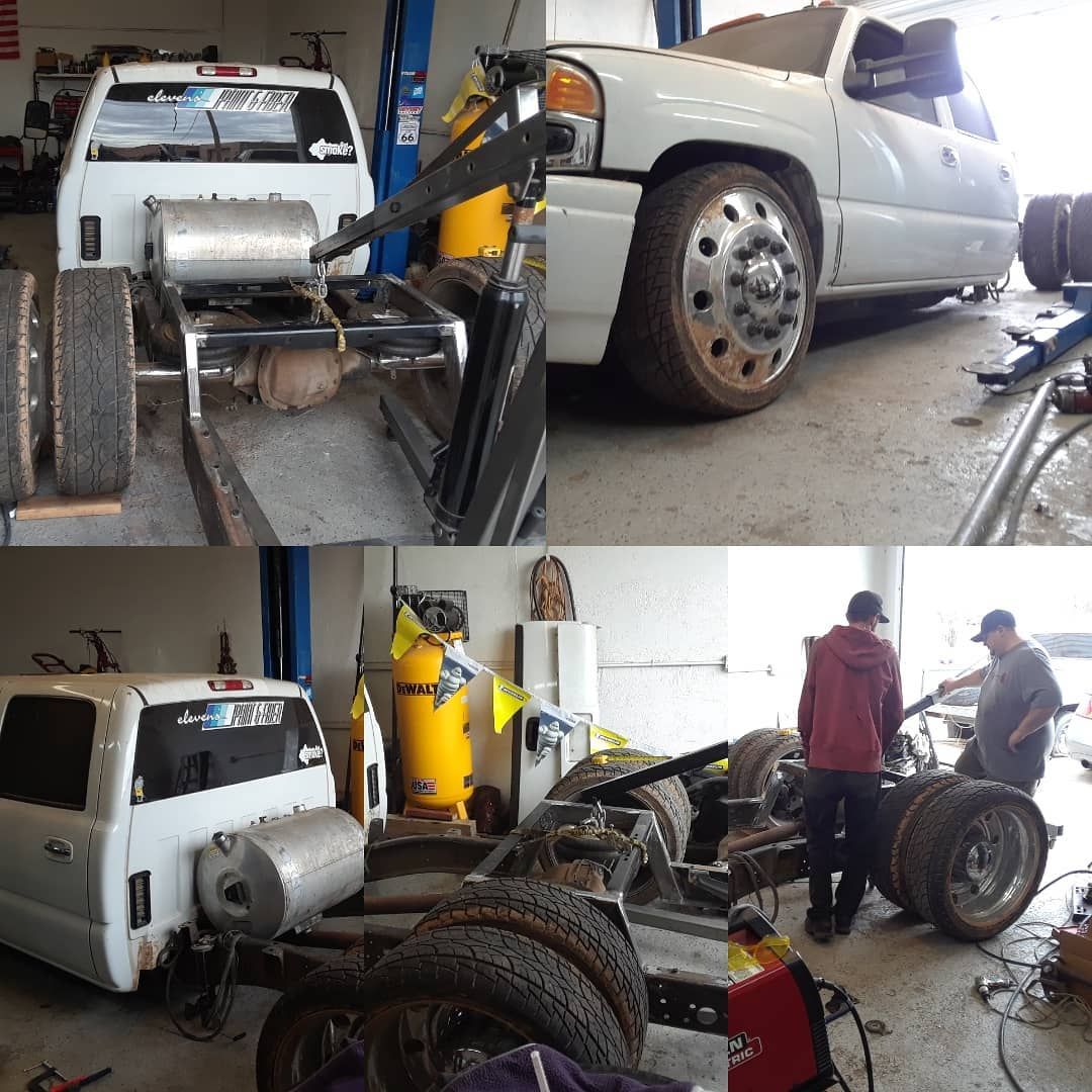 White truck undergoing modifications in a garage. Two men work on the chassis, with the truck bed removed.