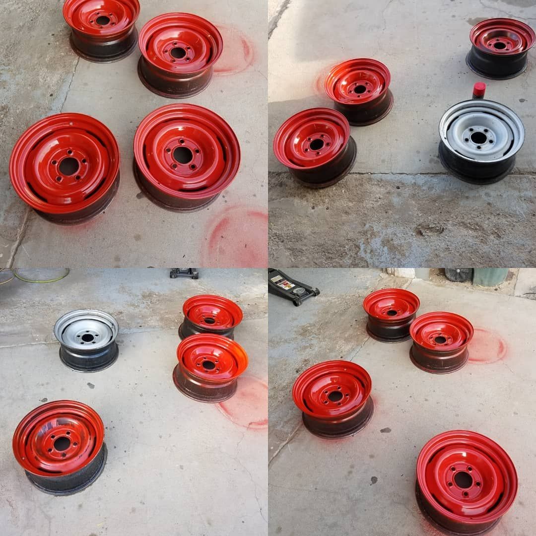 A collection of red car rims are laid out on a concrete surface, some stacked, and one rim is silver.