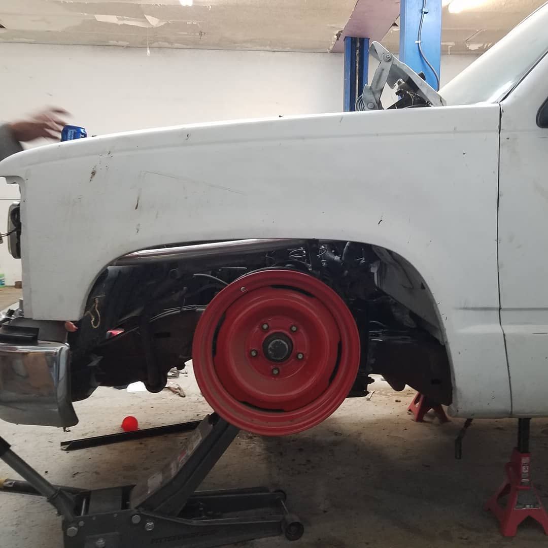 White truck with a red wheel raised on a jack, inside a garage.