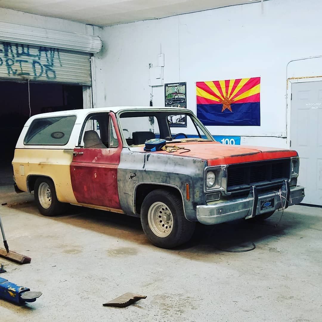 A weathered, multi-colored Chevy Blazer in a garage with an Arizona flag hanging in the background.