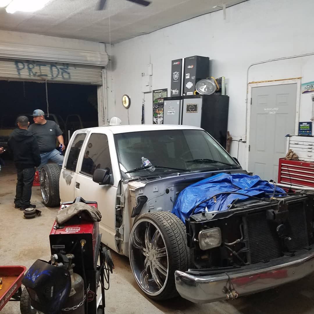 White truck with missing body panels inside a garage, people working on it.