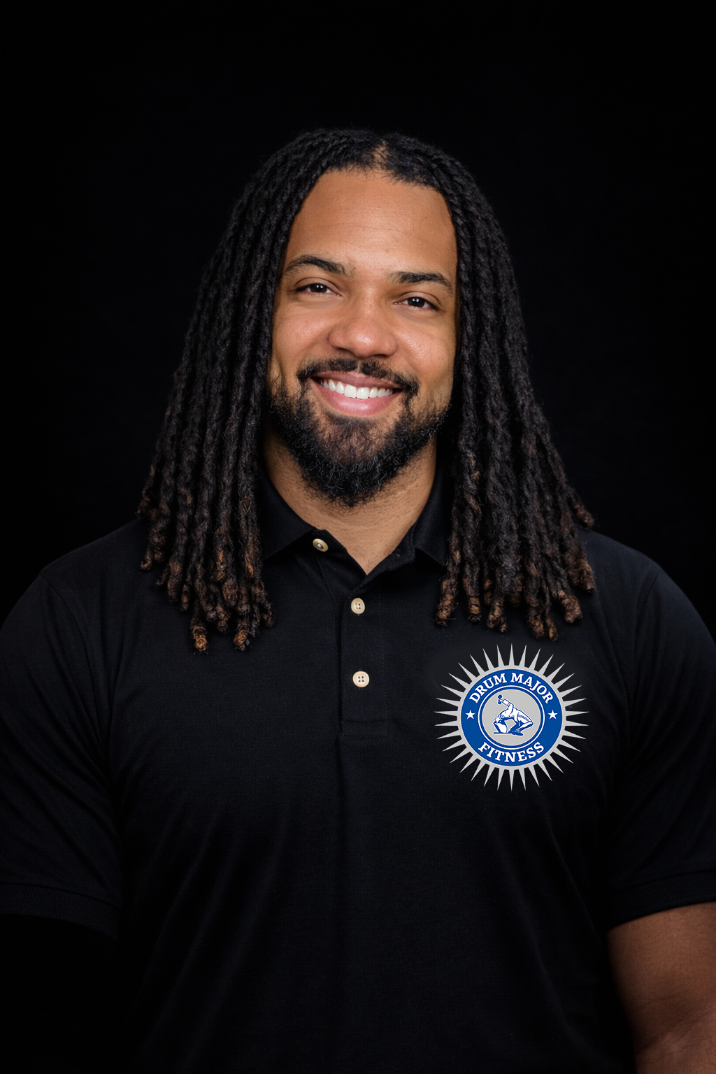 A smiling person with dreadlocks wearing a black polo shirt with a circular sunburst logo against a black background.
