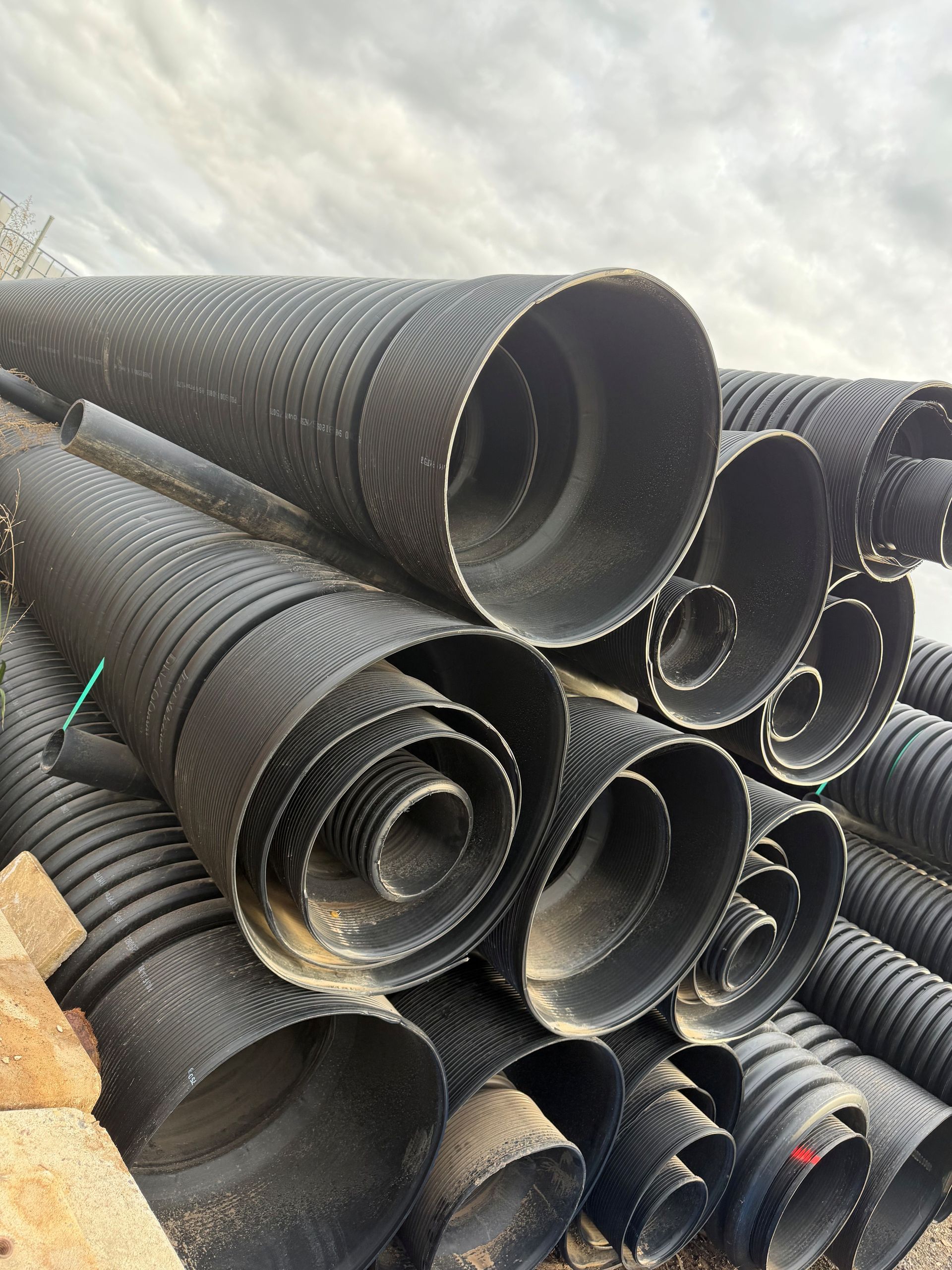 Stacked black corrugated drainage pipes outdoors, bundled and piled in rows. — Dampier Street Landscape Supplies in Taminda, NSW