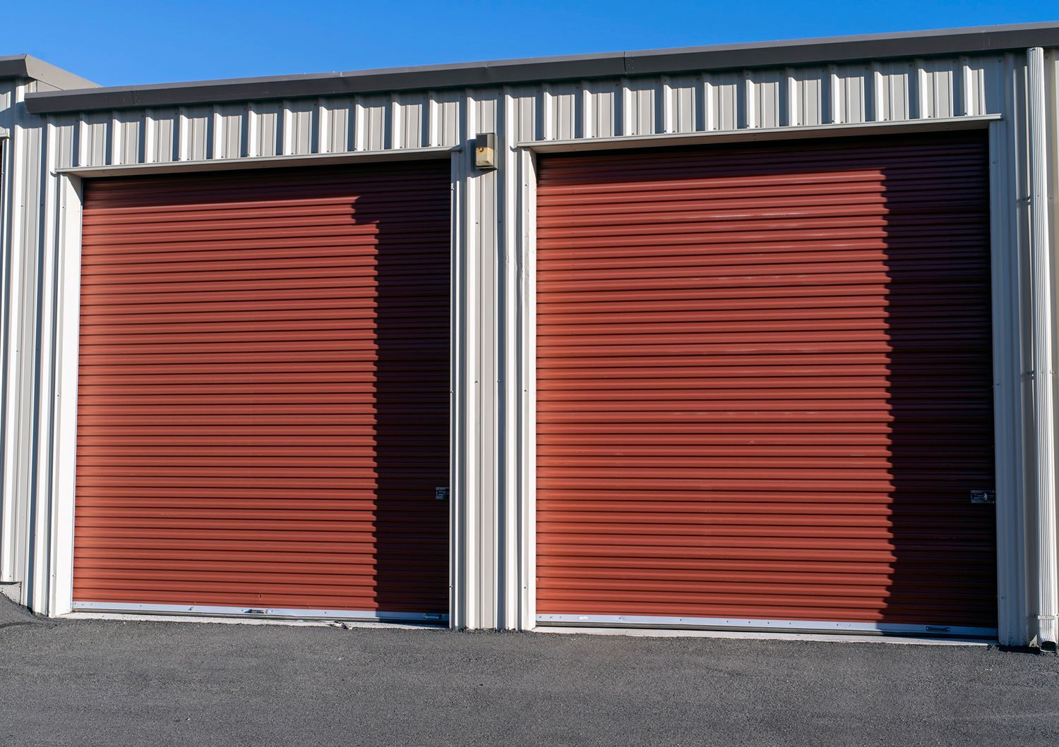 Two red roll-up storage unit doors, bordered by white metal, against a blue sky.