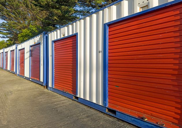 Row of white and blue storage units with red doors, outdoors.