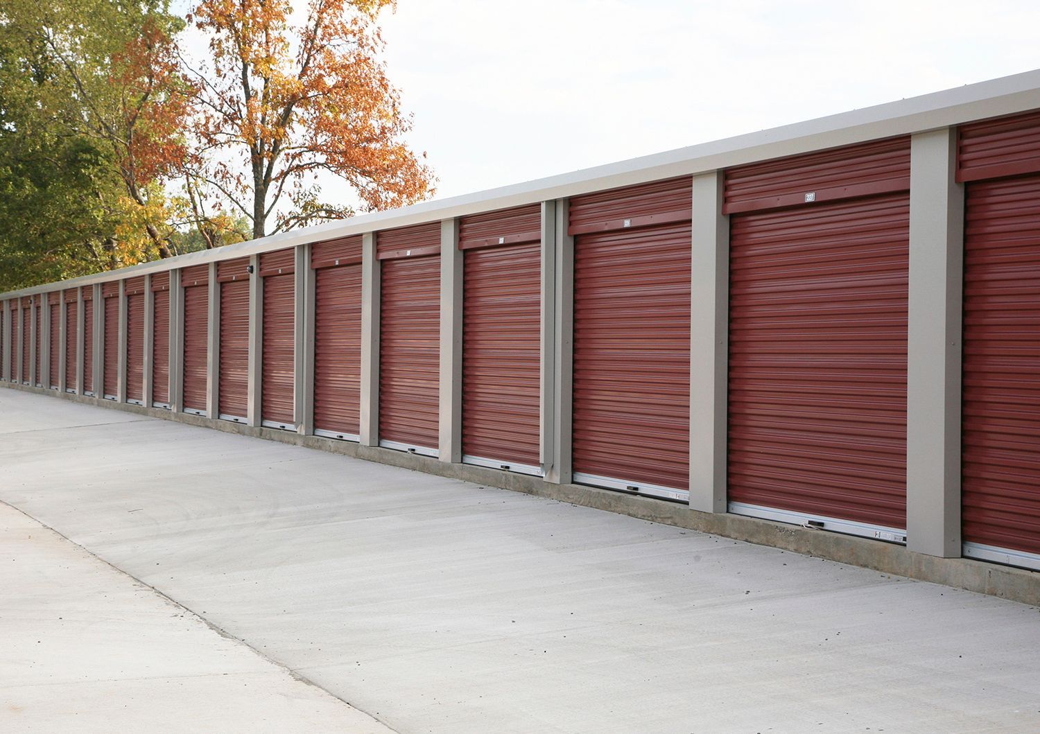 A long, brown and gray sound barrier along a concrete path with autumn trees in the background.