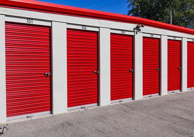 Red storage unit doors with white frames and red trim. Gravel ground.