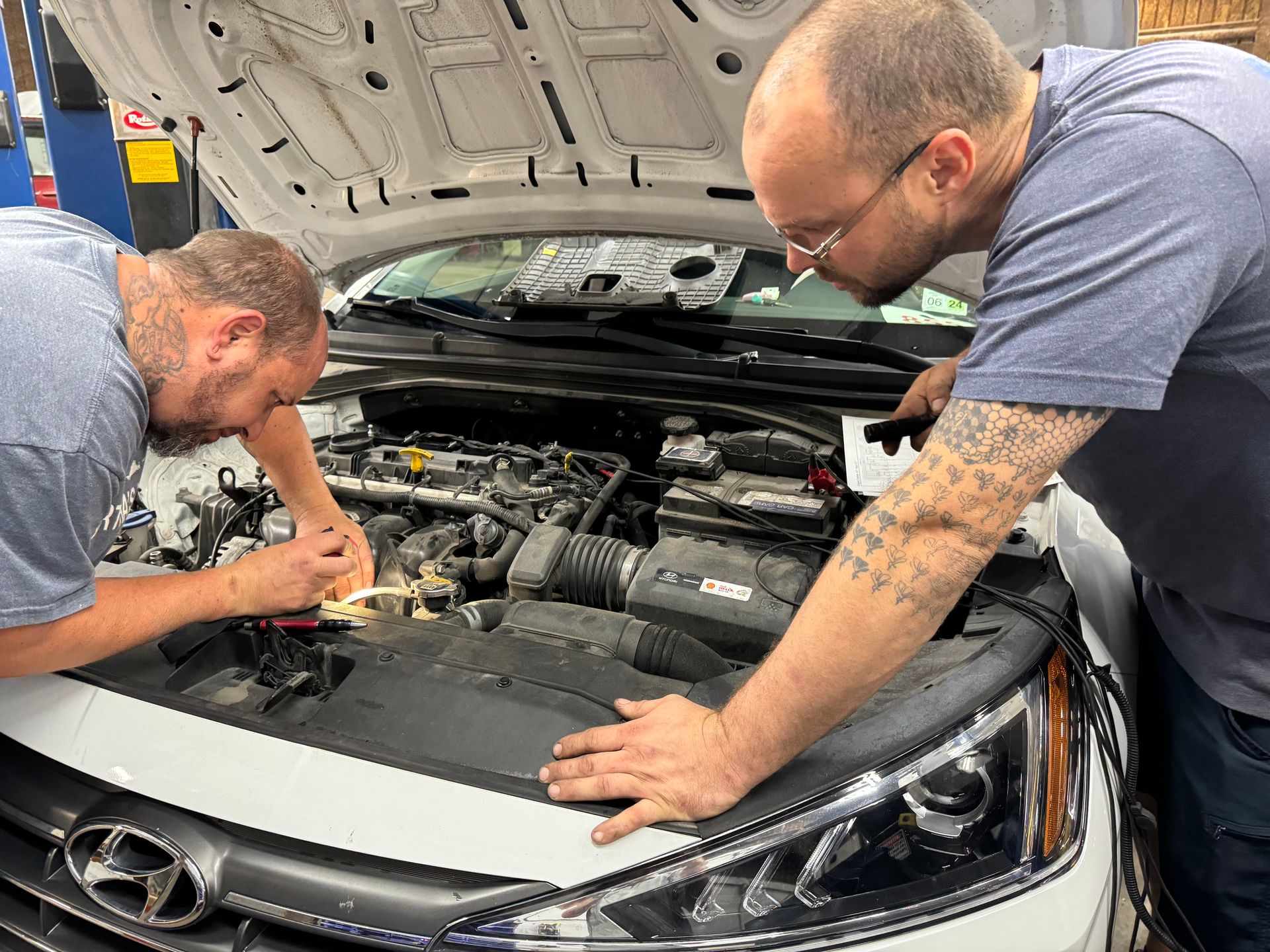 Two mechanics working on the engine of a white car in a garage. | Sonny's Auto Repair