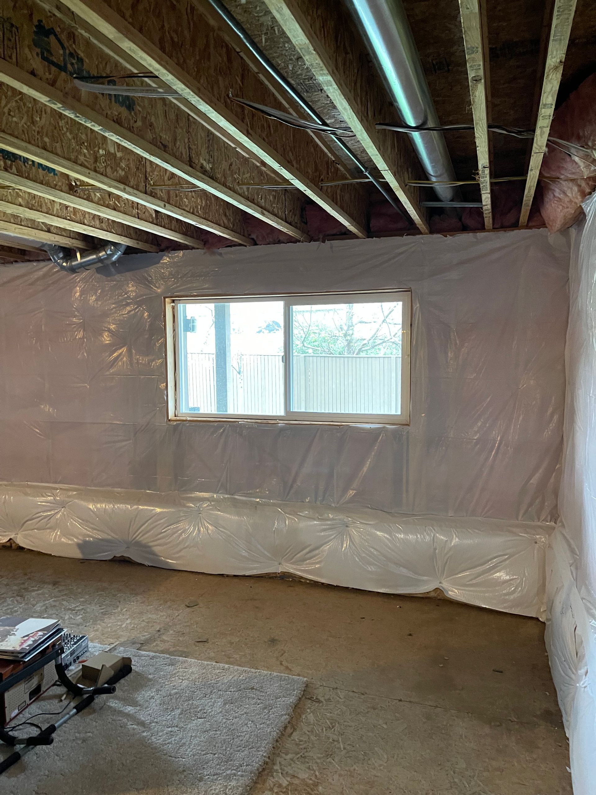 A basement with a window and plastic covering the walls.