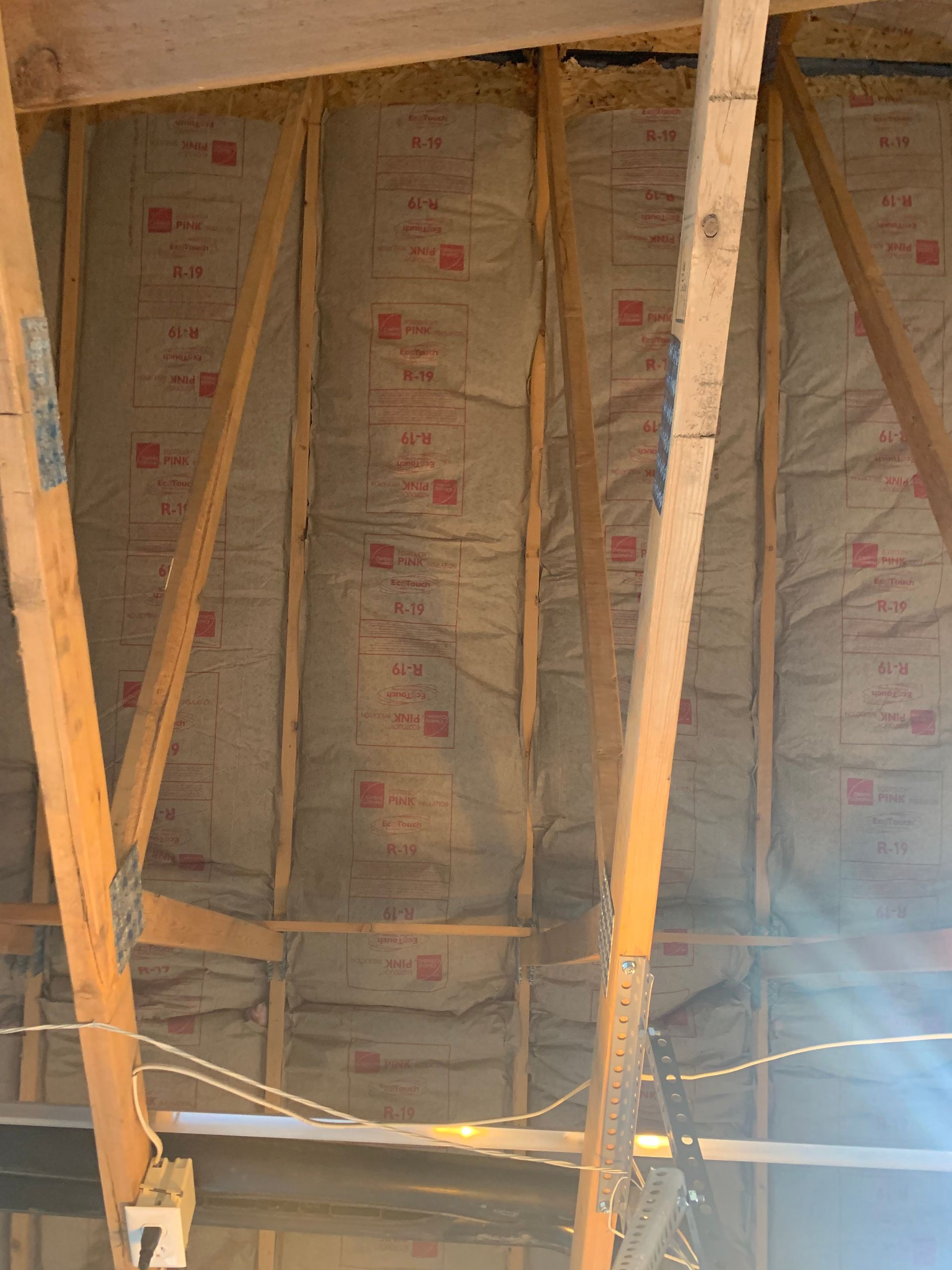 The ceiling of a building with wooden beams and insulation.