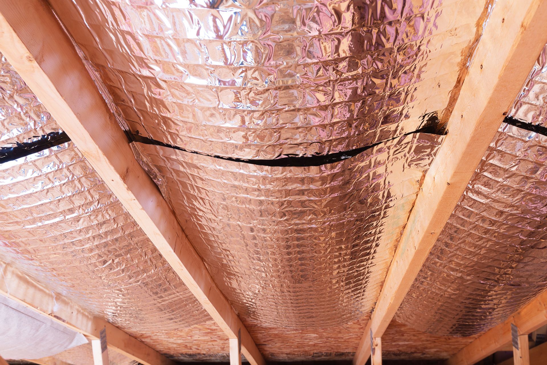 A close up of a ceiling with aluminum foil and wooden beams.