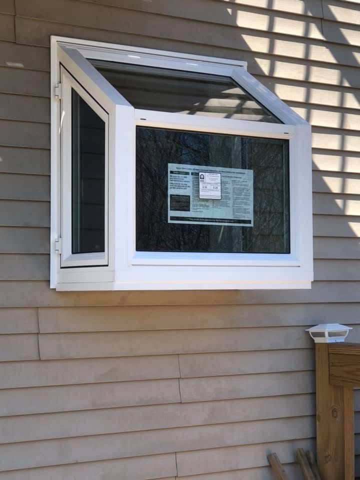 White, angled window on a beige-sided building, partially open.  A sheet of newspaper is visible inside the window.