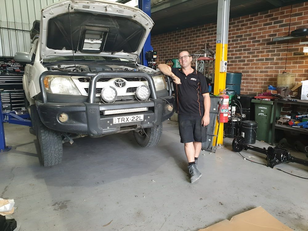 A Man Is Standing In Front Of 4x4 Repairing In A Garage  — 100% Automotive In South Nowra, NSW