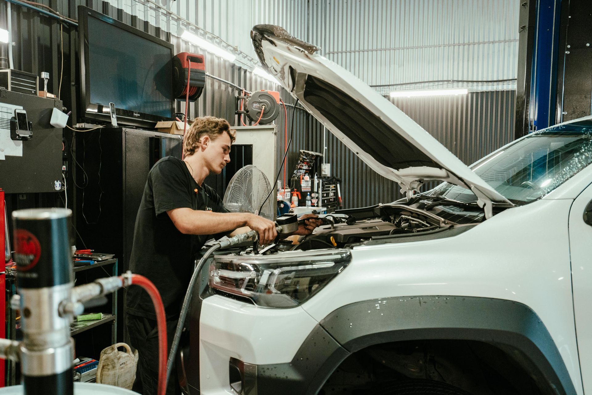 Mechanic working on the engine of a white truck in a garage; hood open, using tools. — 100% Automotive In South Nowra, NSW