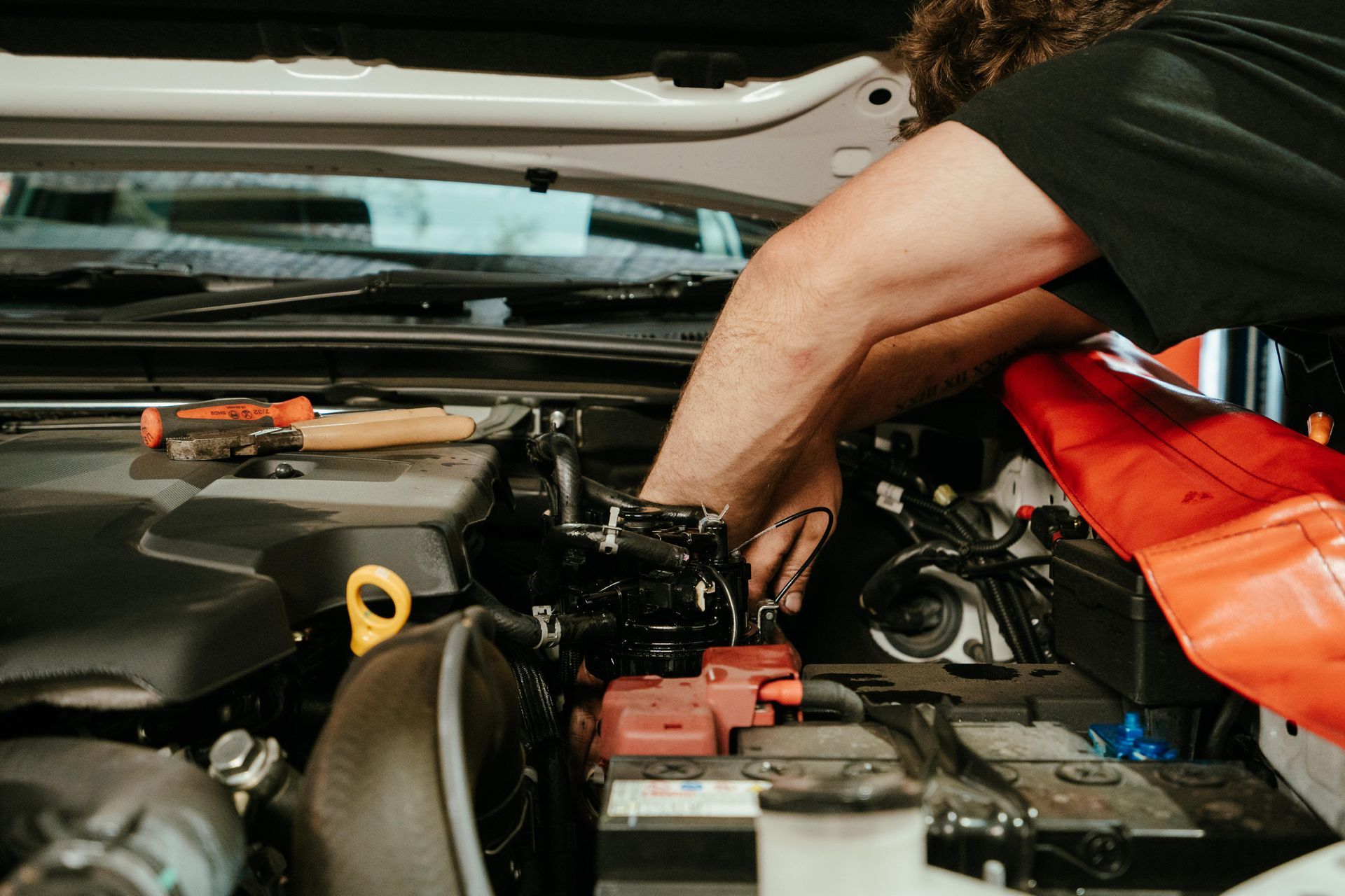Mechanic working on car engine, reaching inside with hands. Battery and tools visible. — 100% Automotive In South Nowra, NSW