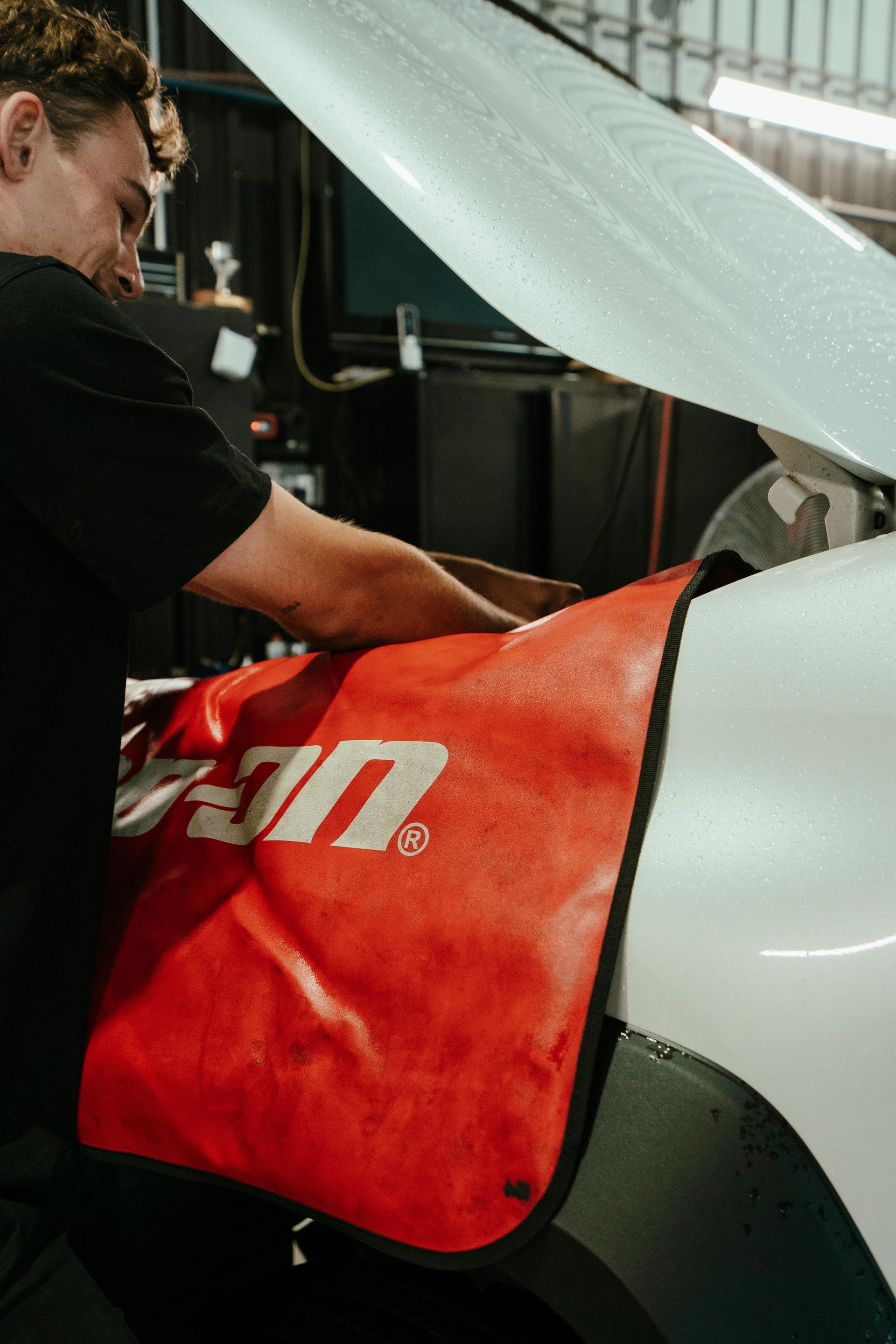 Mechanic working on a car engine  with a red Snap-on fender cover. — 100% Automotive In South Nowra, NSW