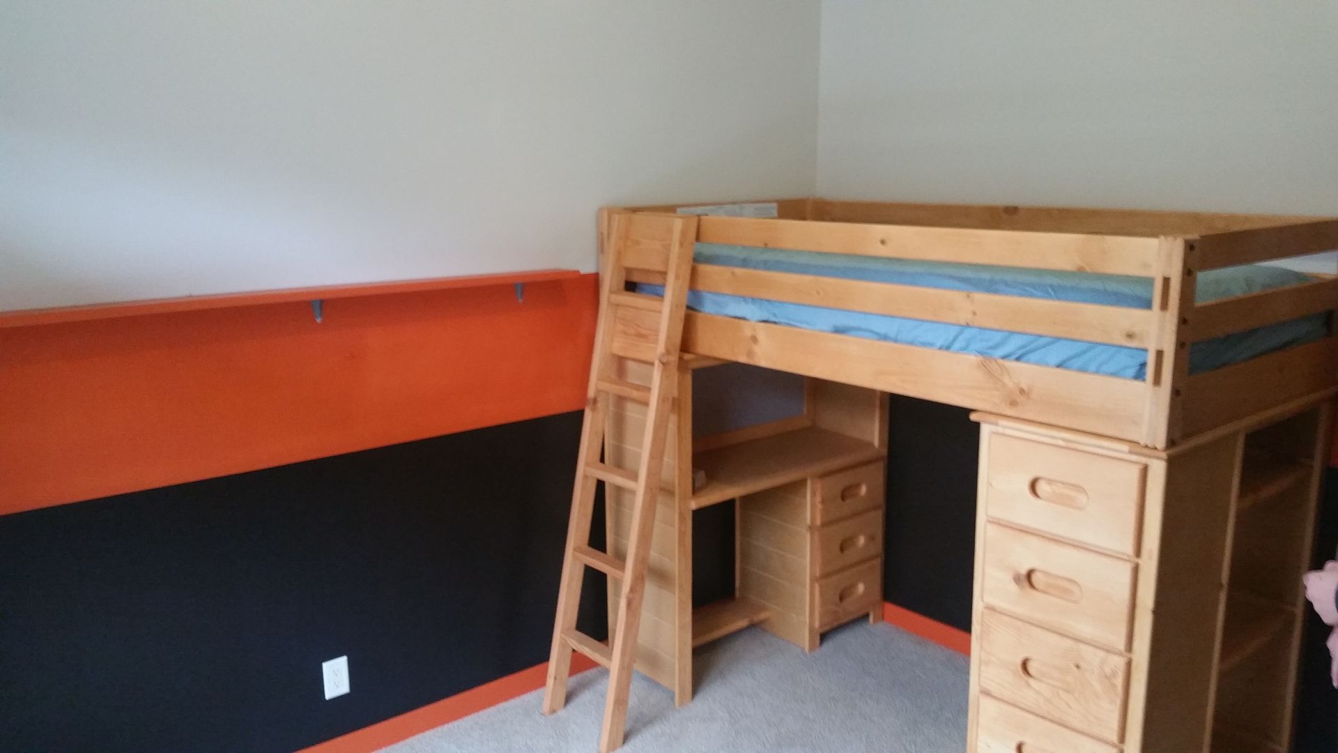 Wooden loft bed with ladder and desk in a small room with orange and black walls
