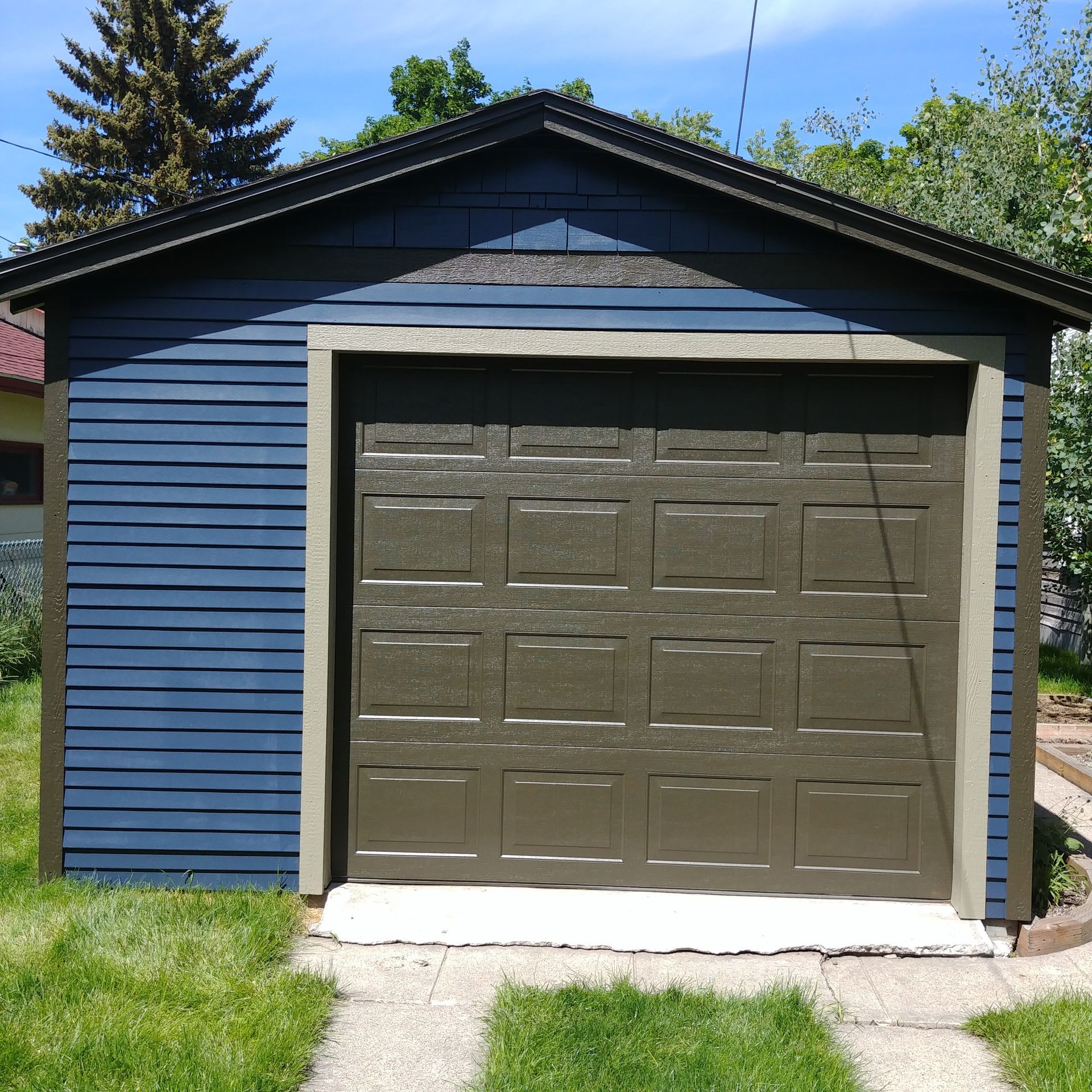 Blue garage with a brown door and white trim, seen from the front on a sunny day