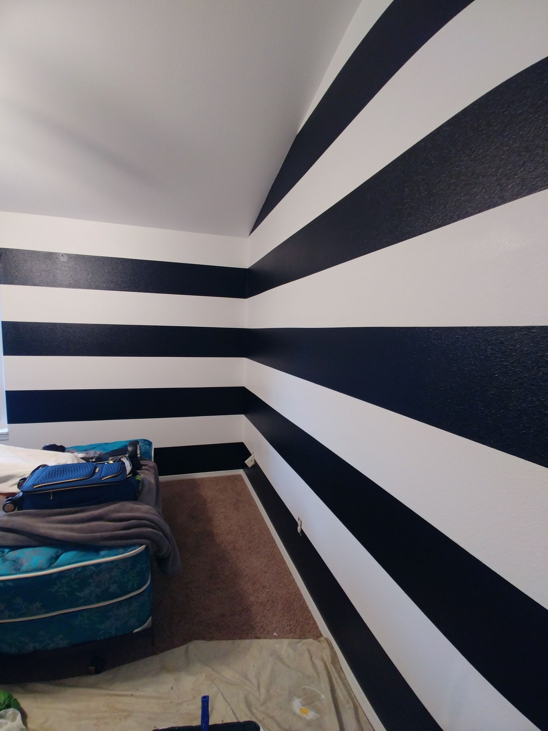 A room with black-and-white striped walls and a bed in the corner on a light floor.