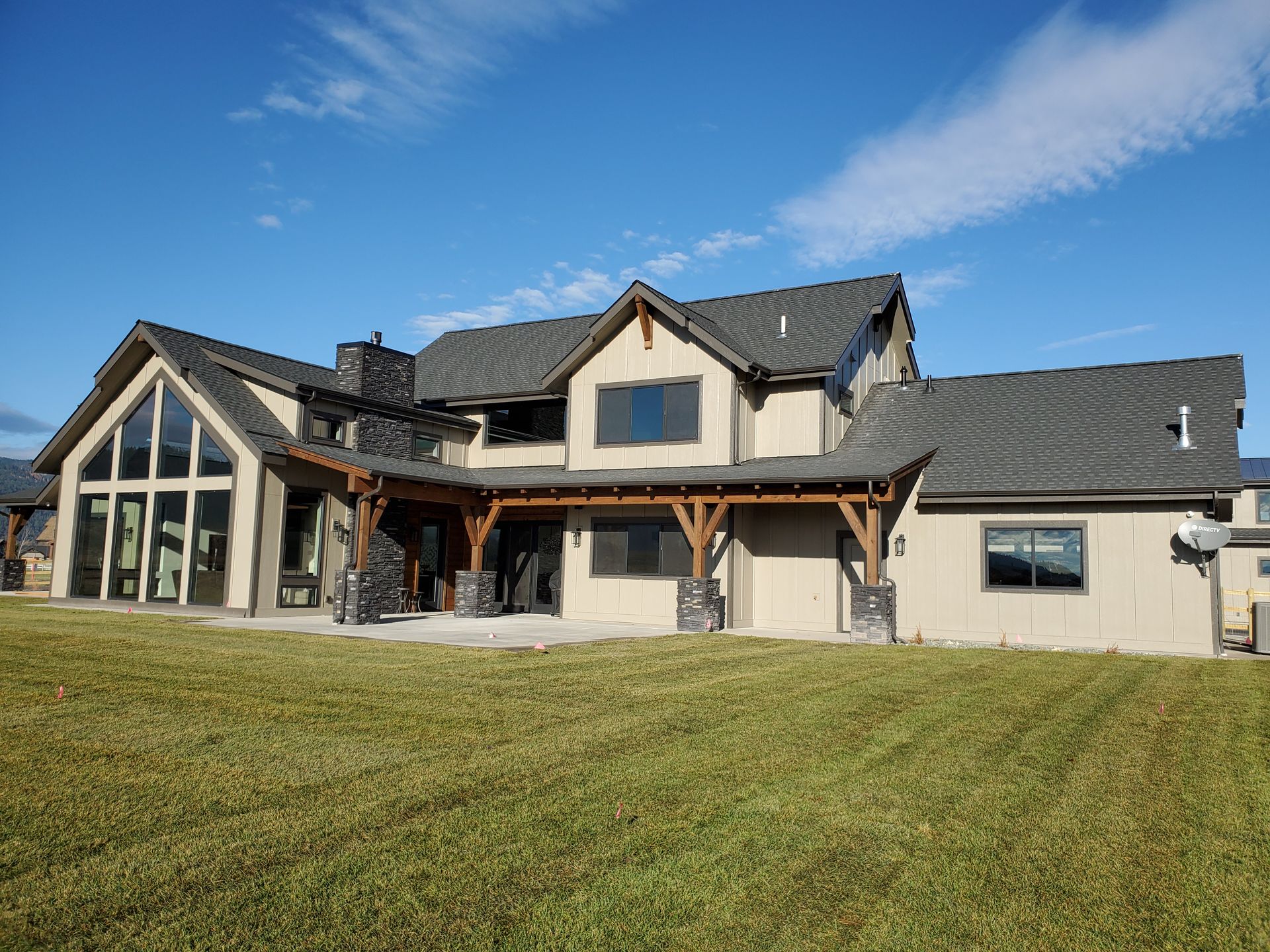 Large modern house with a stone-and-wood facade and a wide lawn under a blue sky