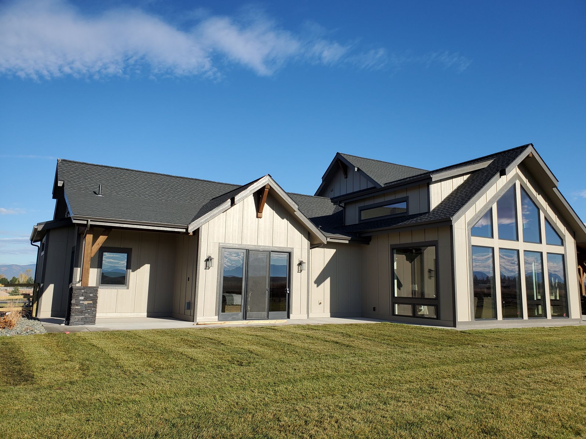 Modern house exterior with large windows, dark roof, and a grassy lawn under a blue sky