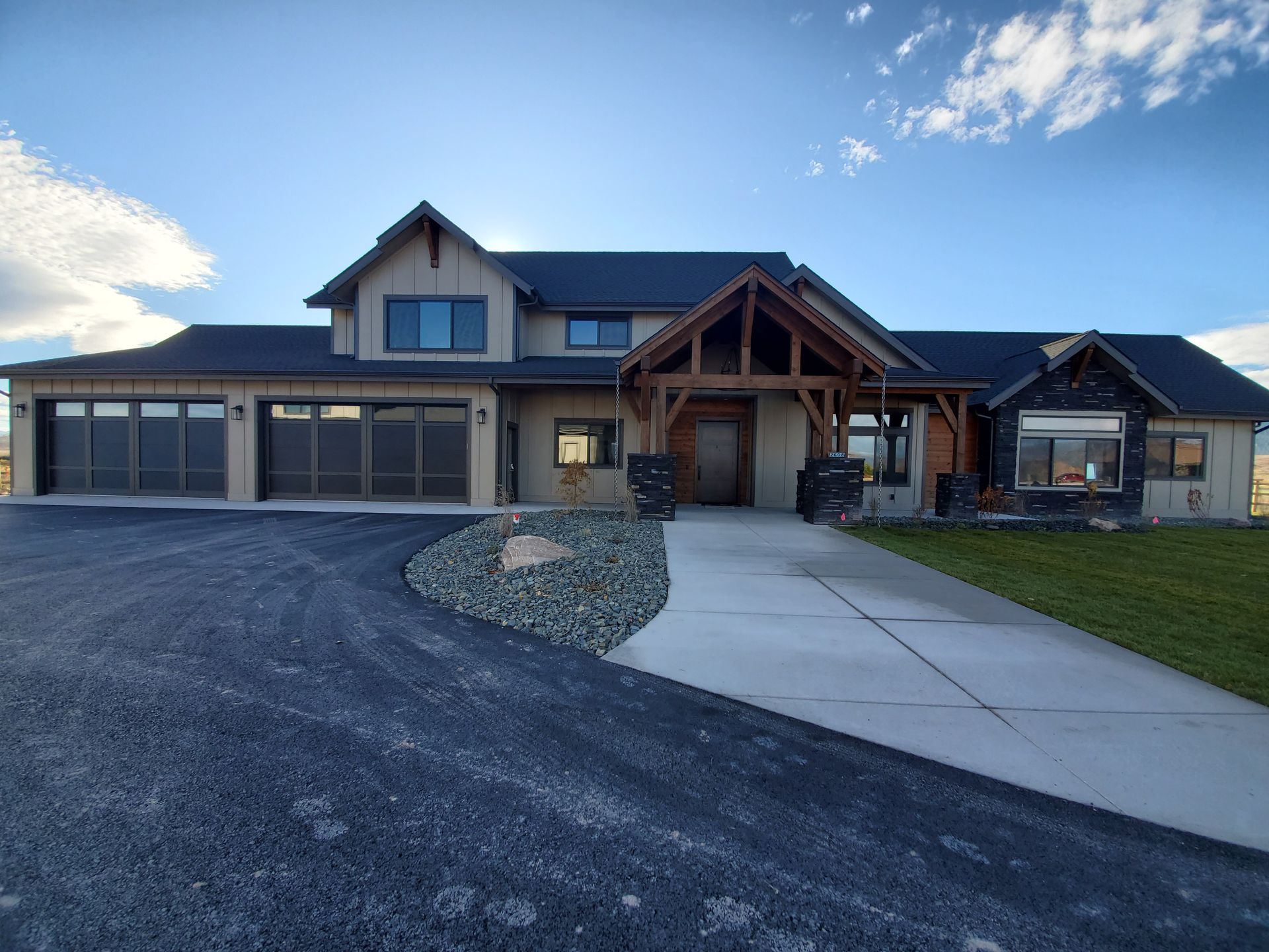 Modern house with a three-car garage, front walkway, and gravel driveway under a blue sky