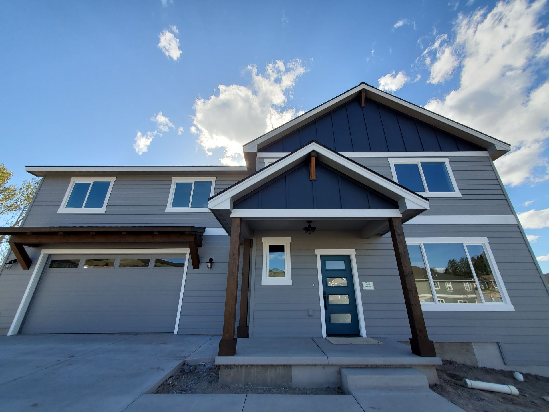 Modern beige barn-style building with dark roof and large garage doors on a gravel lot under a blue sky