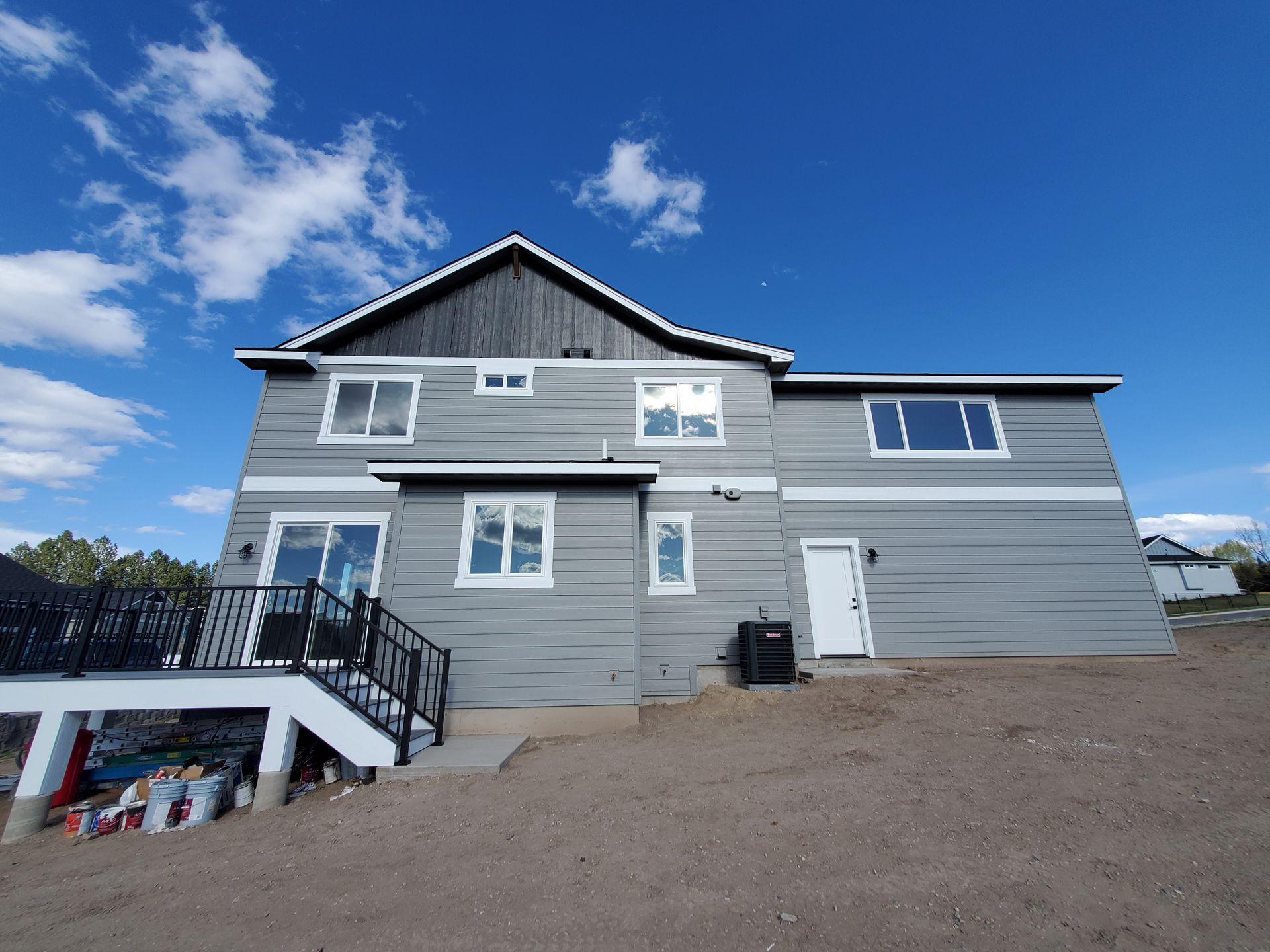 Gray two-story house with black roof, white-trimmed windows, and a front staircase under a blue sky