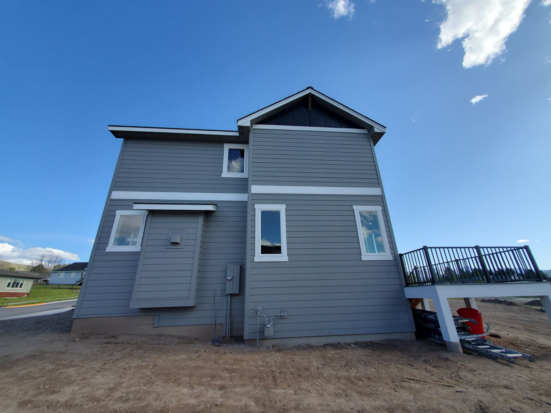 Gray two-story house under construction with blue sky, white trim, and a small deck on the right.