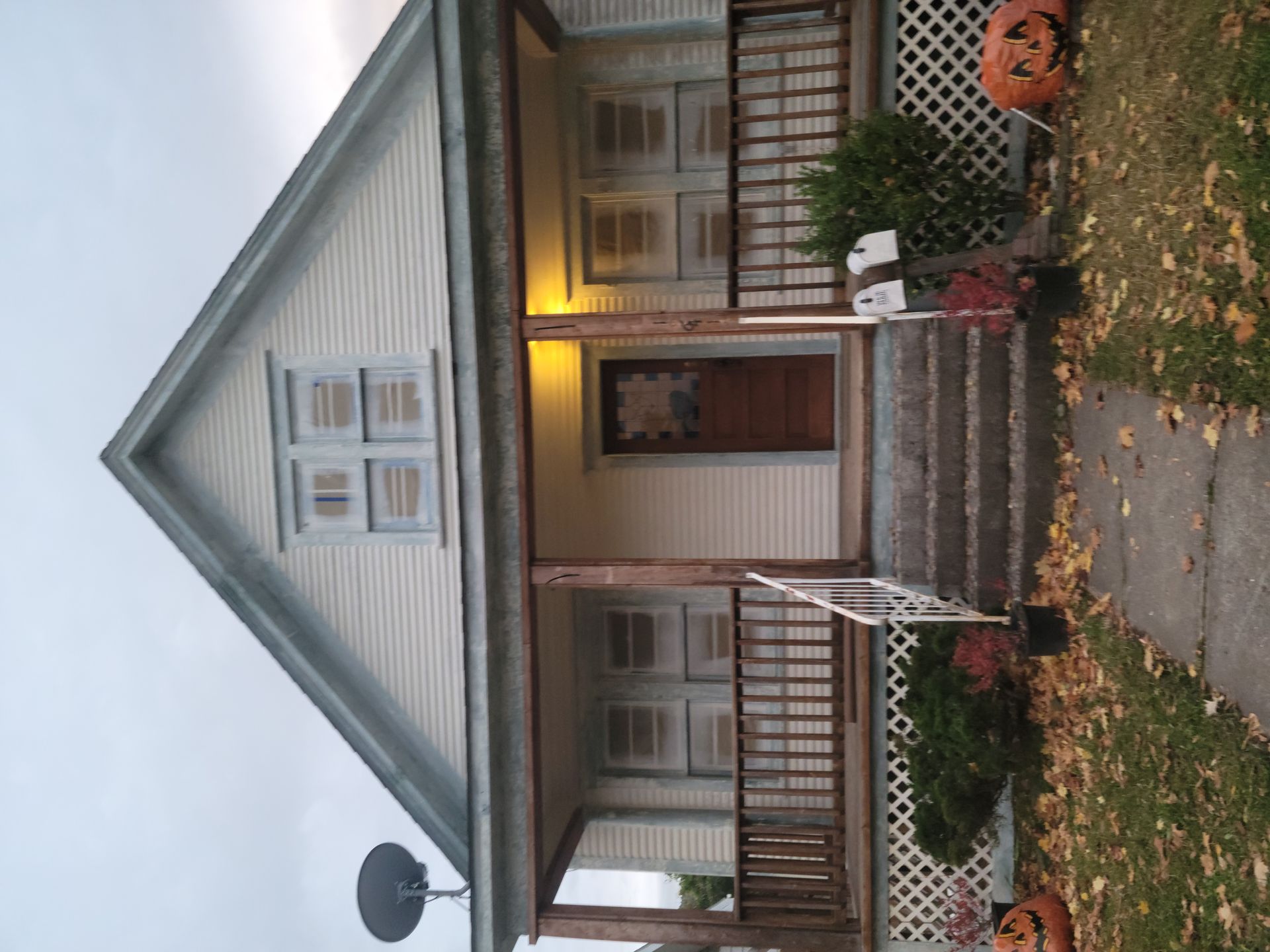 Small gray house with a front porch, lit doorway, and steps leading to a sidewalk and yard.