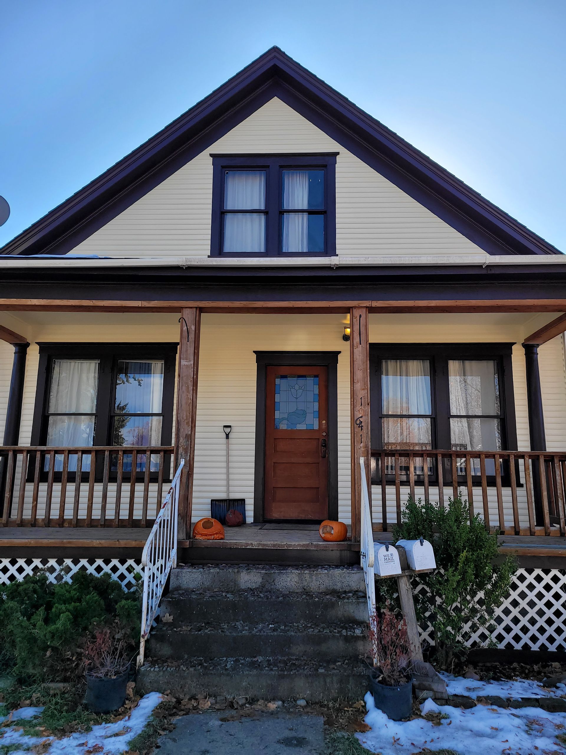 Front view of a beige house with dark trim, a porch, steps, and a centered wooden door