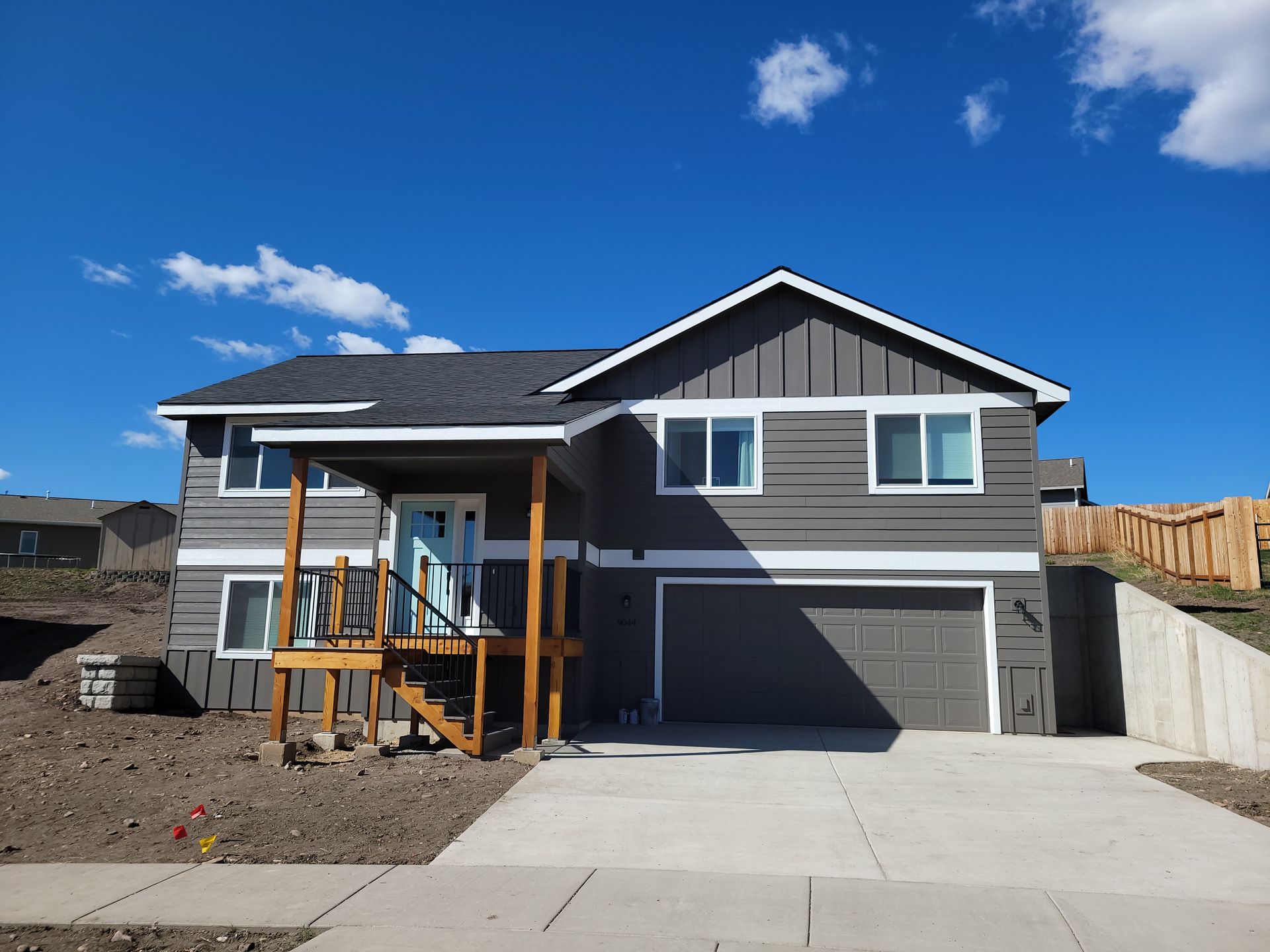 New gray two-story house with a front porch and garage under a blue sky