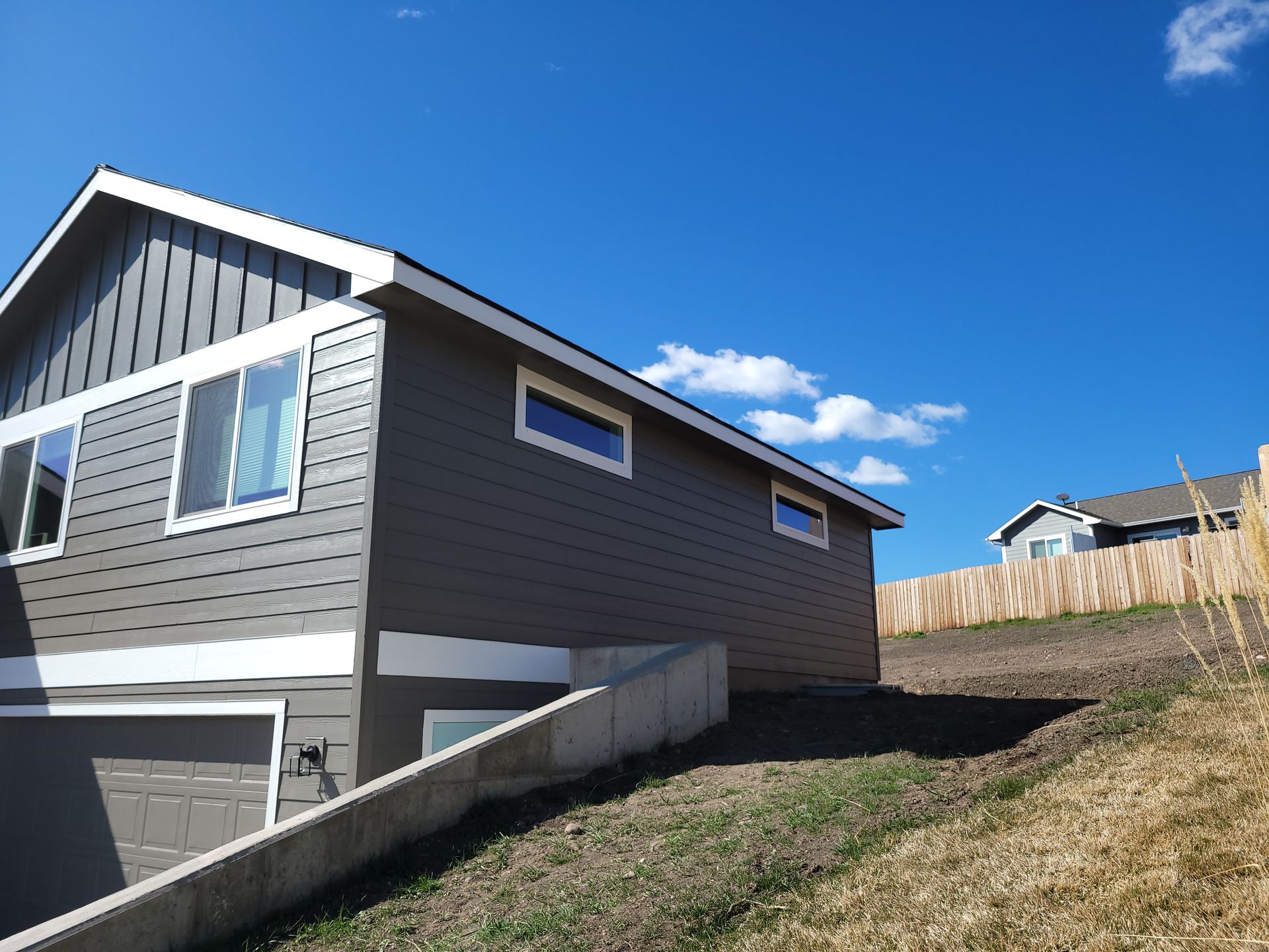 Gray house with white trim on a sloped yard under a bright blue sky