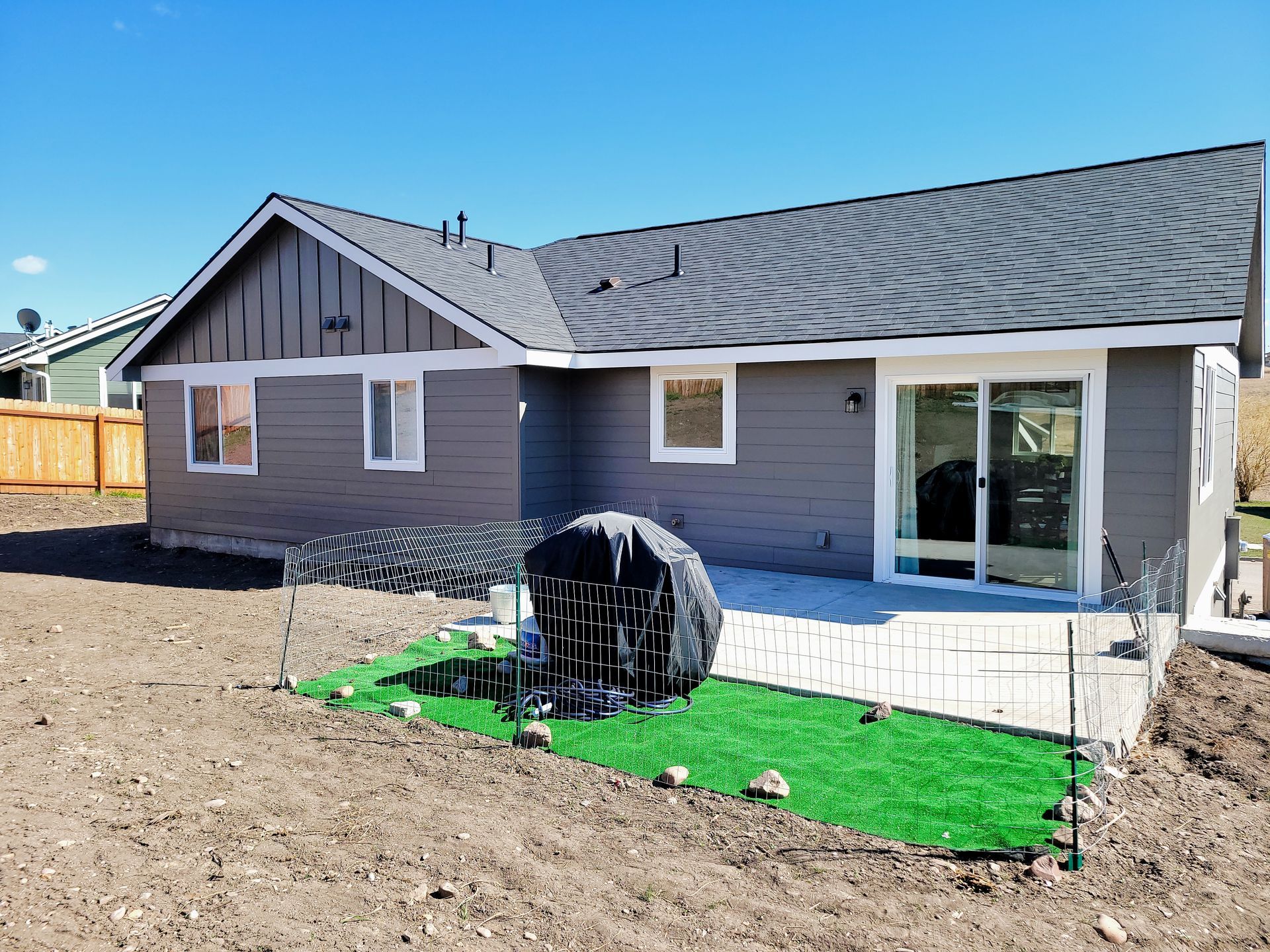 Backyard view of a gray house with sliding glass door and a small green turf area with a black fire pit.