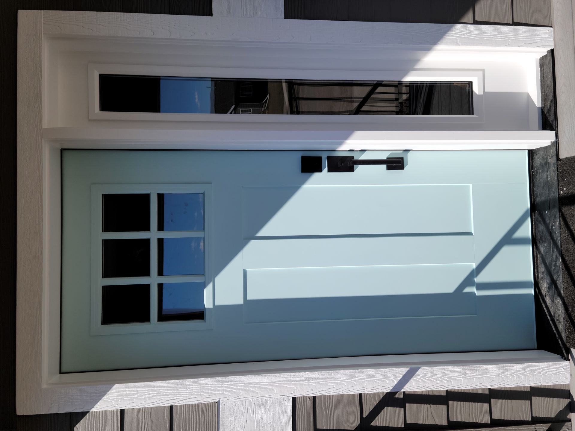 White front door with black hardware and four small window panes, set in a brick entryway.