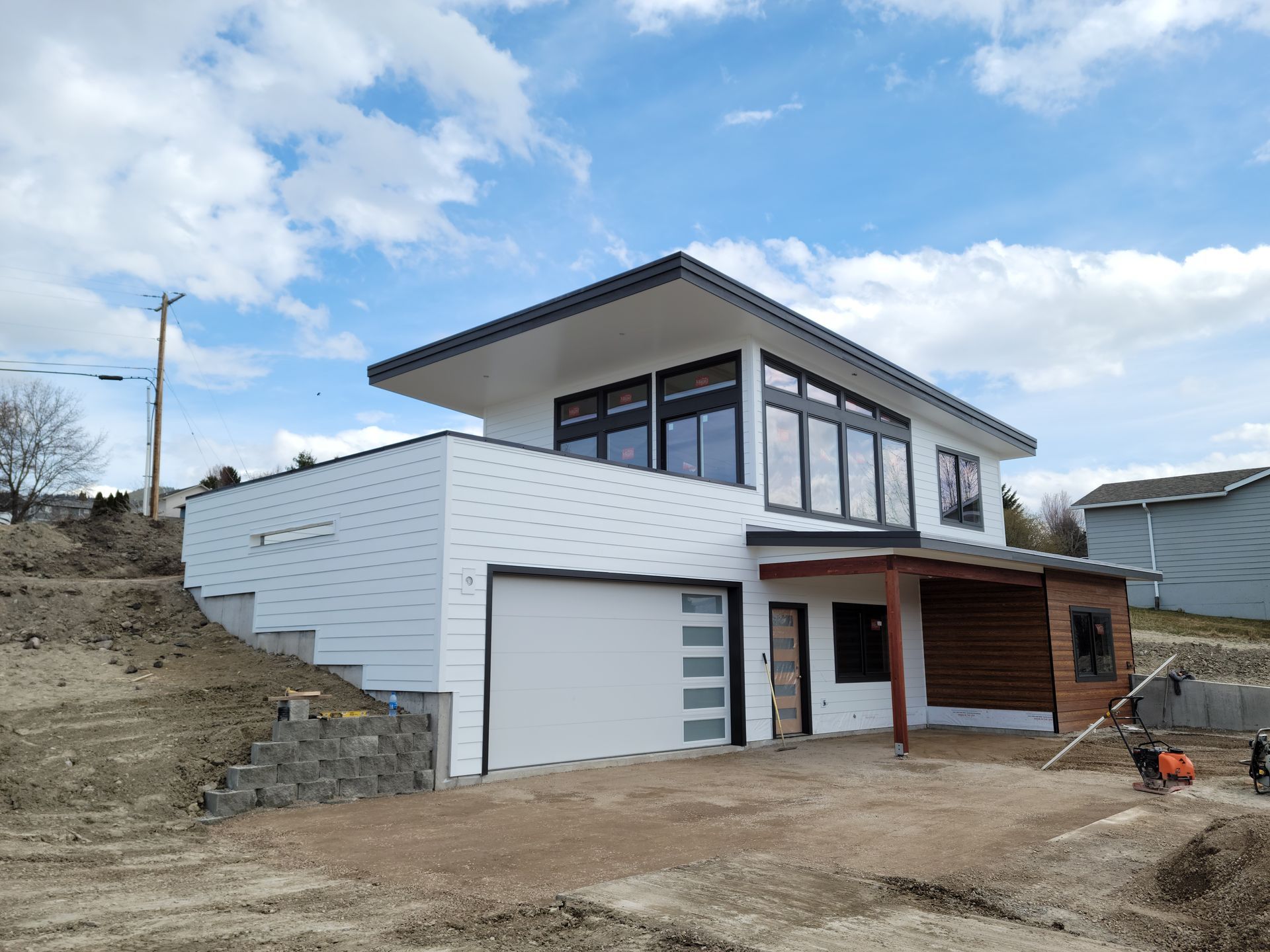 Modern two-story house under construction with white exterior, garage, and wooden porch under a cloudy sky