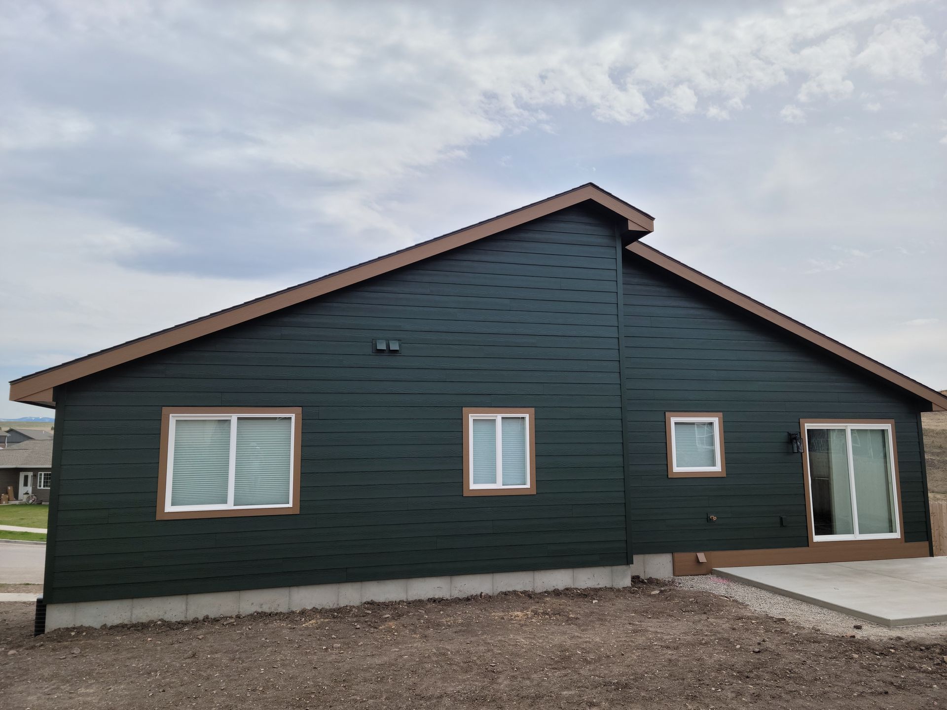 Dark green single-story house with a sloped roof, white-trimmed windows, and a concrete entryway