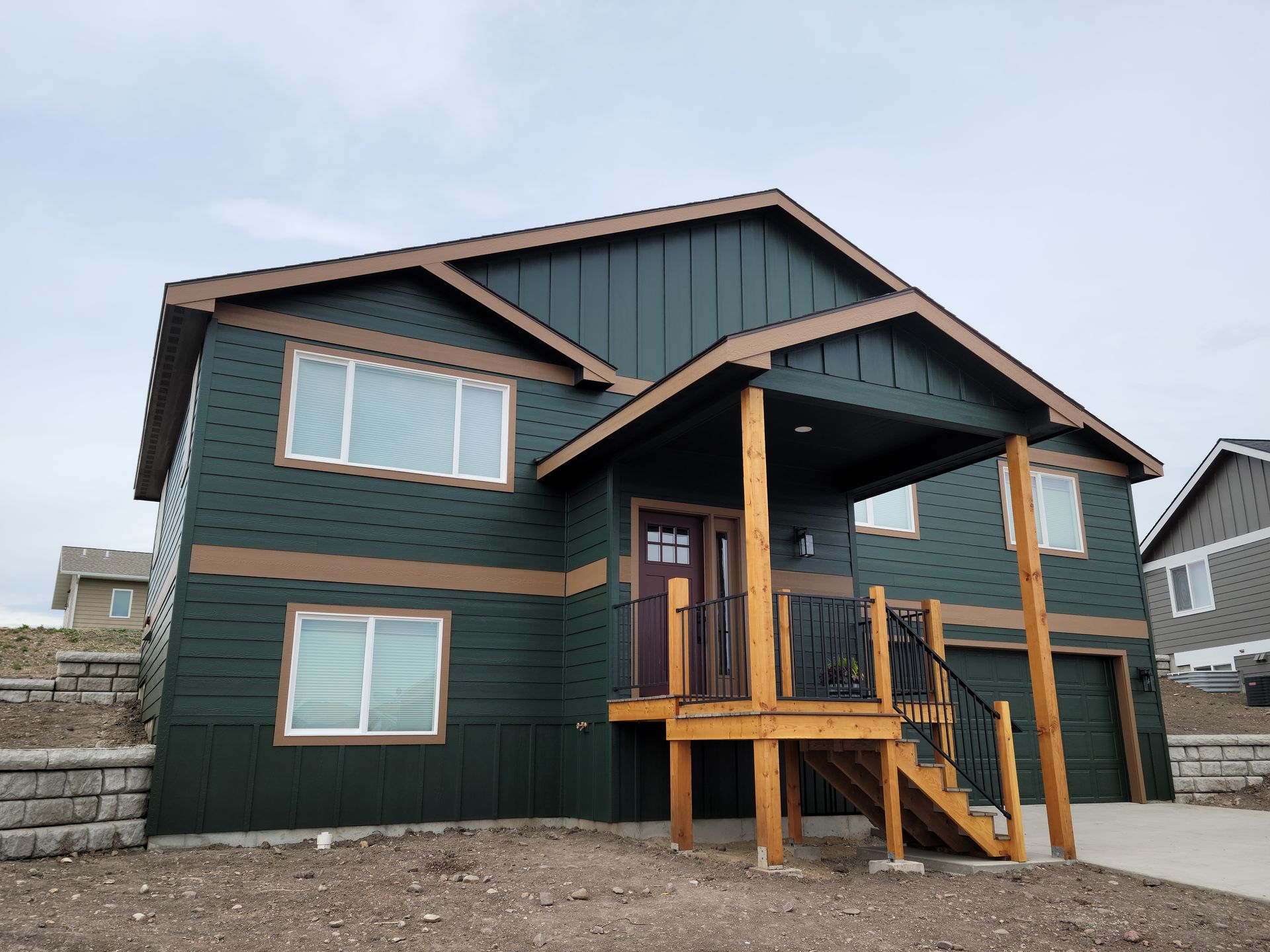 Modern dark green house with wood trim and a covered front porch on a cloudy day