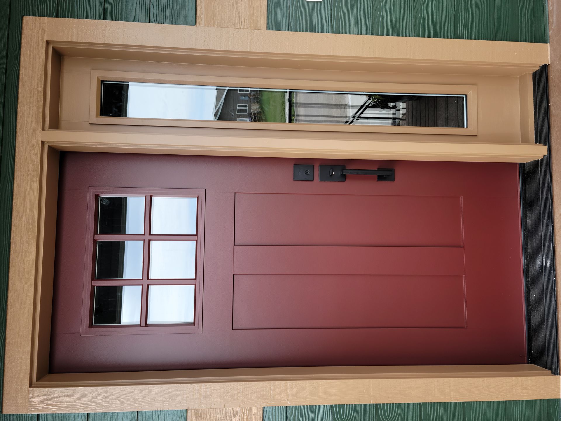 Wooden front door with maroon paneling, narrow glass side window, and decorative trim on a green wall