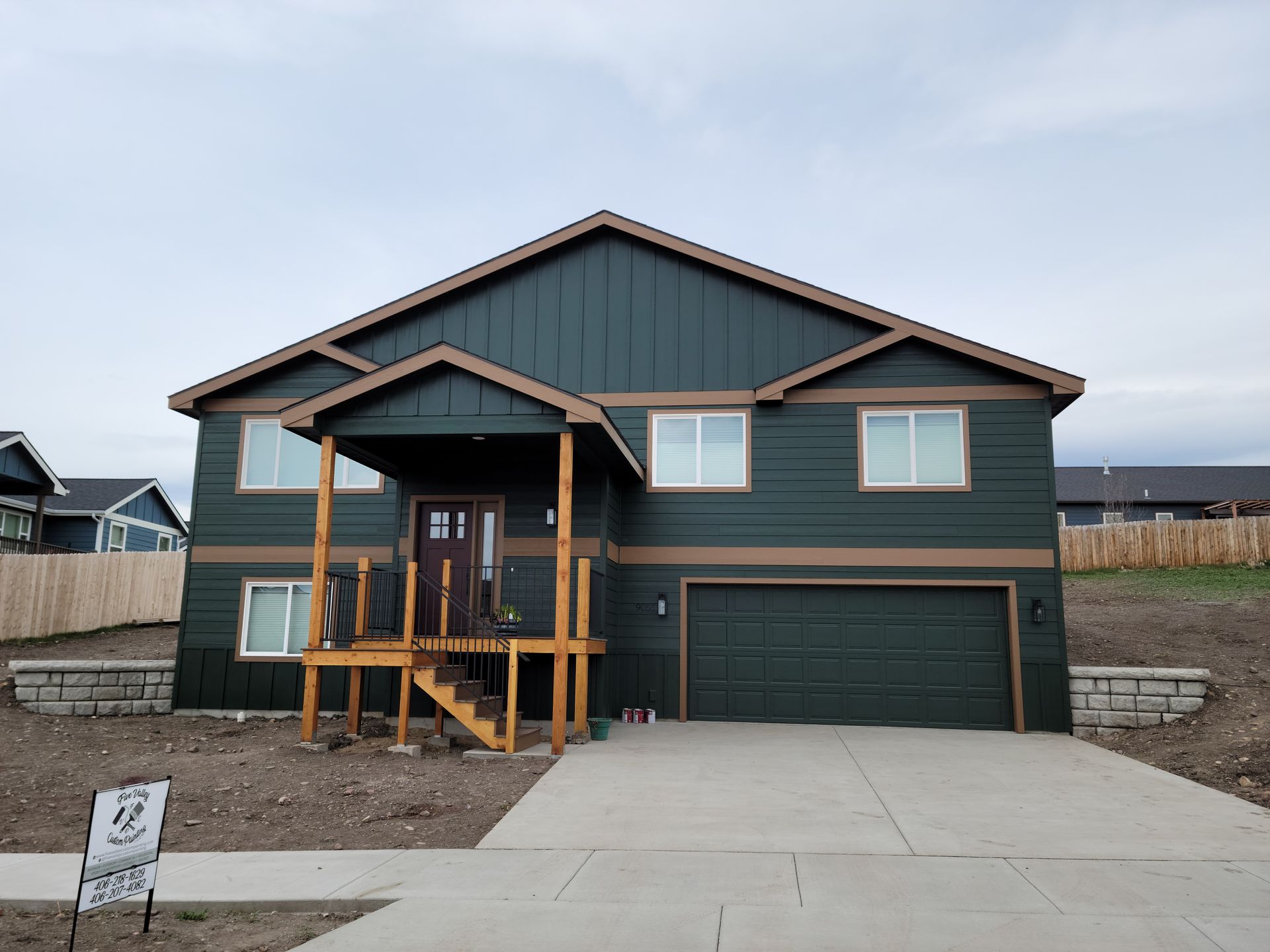 New two-story house with teal siding, tan trim, front porch, and double garage on a concrete driveway.