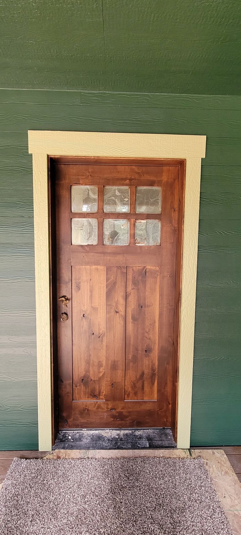 Wooden door with four small windows set in a beige frame against a green wall