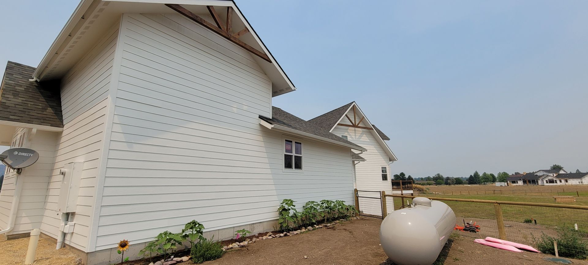 White house exterior with unfinished siding and a large planter in a dirt yard under a cloudy sky