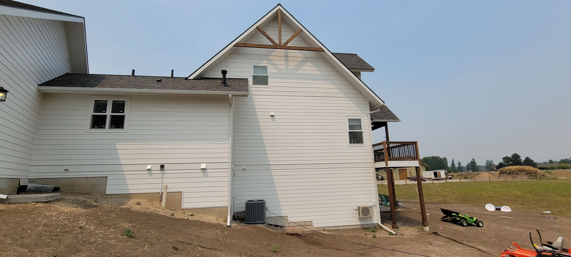 White house exterior under construction with bare ground, windows, and roof framing on a rural lot.