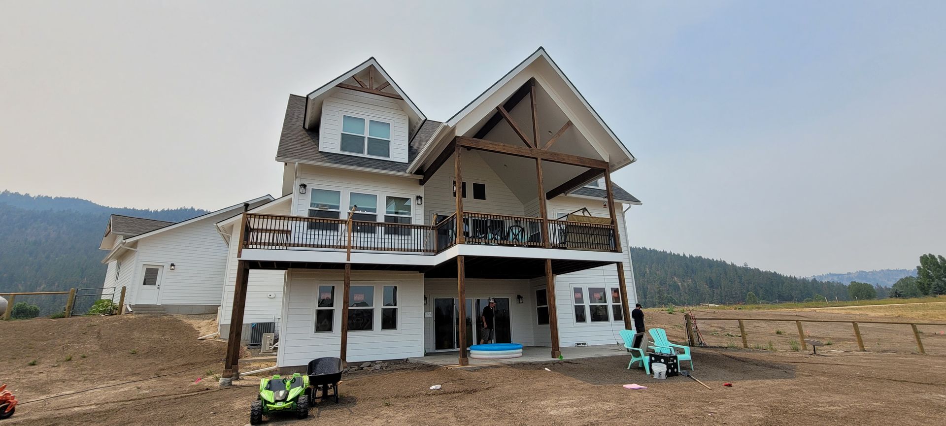 Two-story house under construction in a rural field, with scaffolding and workers outside.