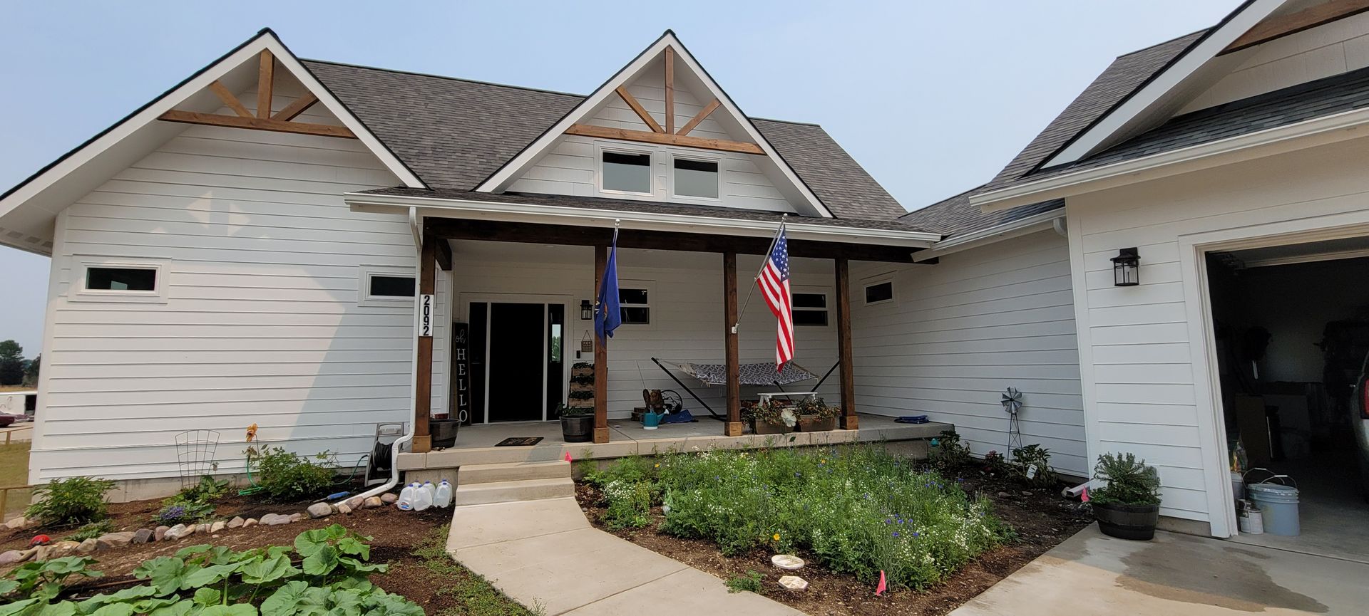 Suburban house exterior with stone facade, front walkway, garden beds, and an American flag by the entrance