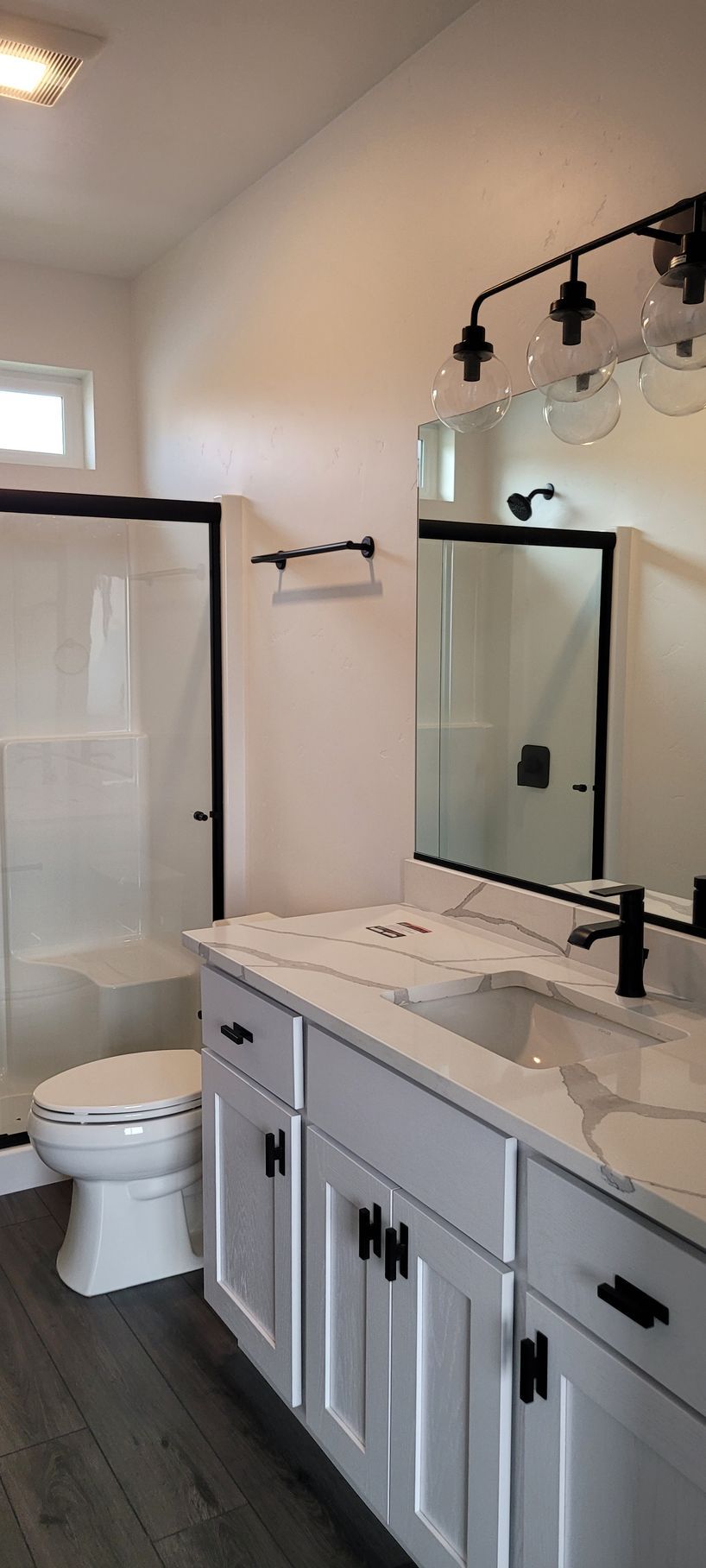 Modern bathroom with white vanity, large mirror, walk-in shower, toilet, and dark wood flooring