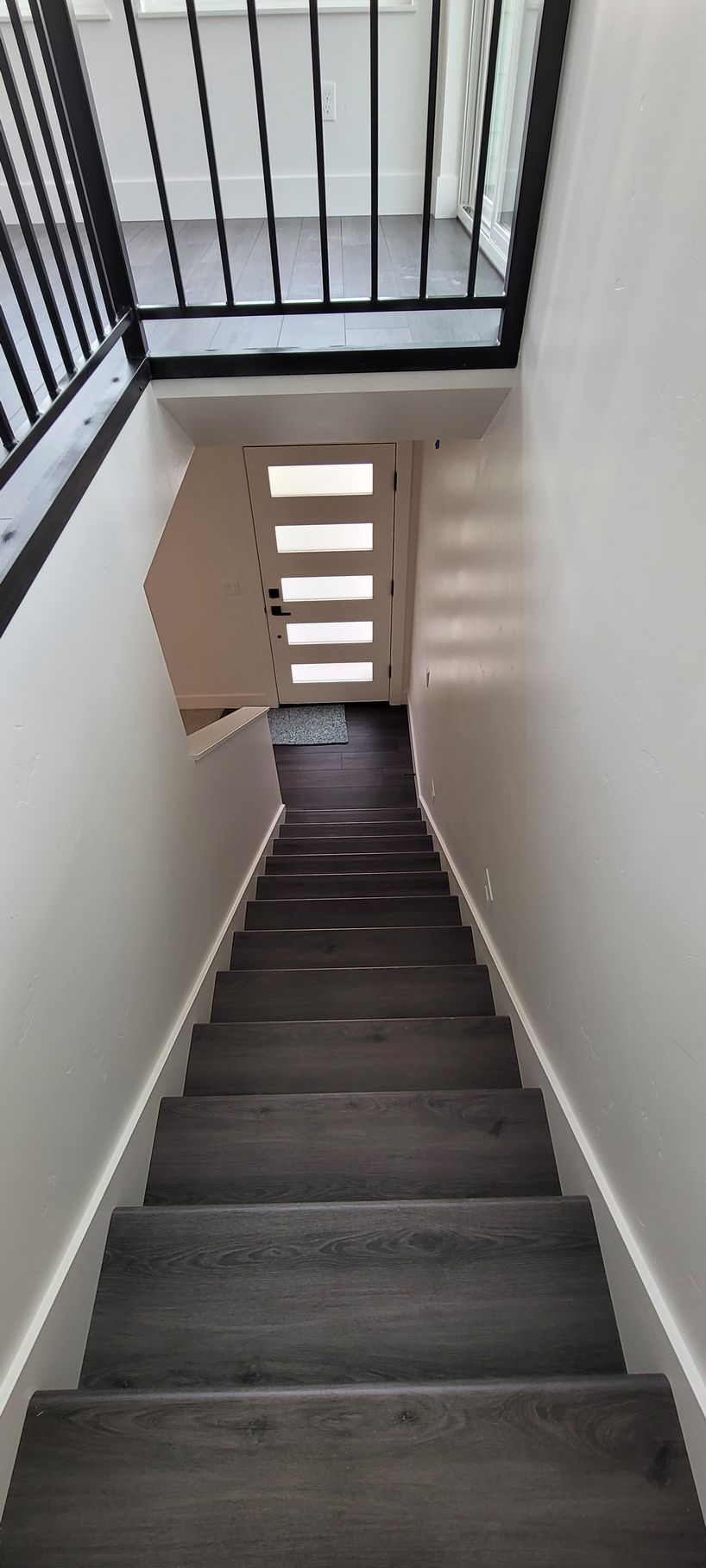 Narrow indoor staircase with dark steps and white walls, viewed upward toward a landing and railing.