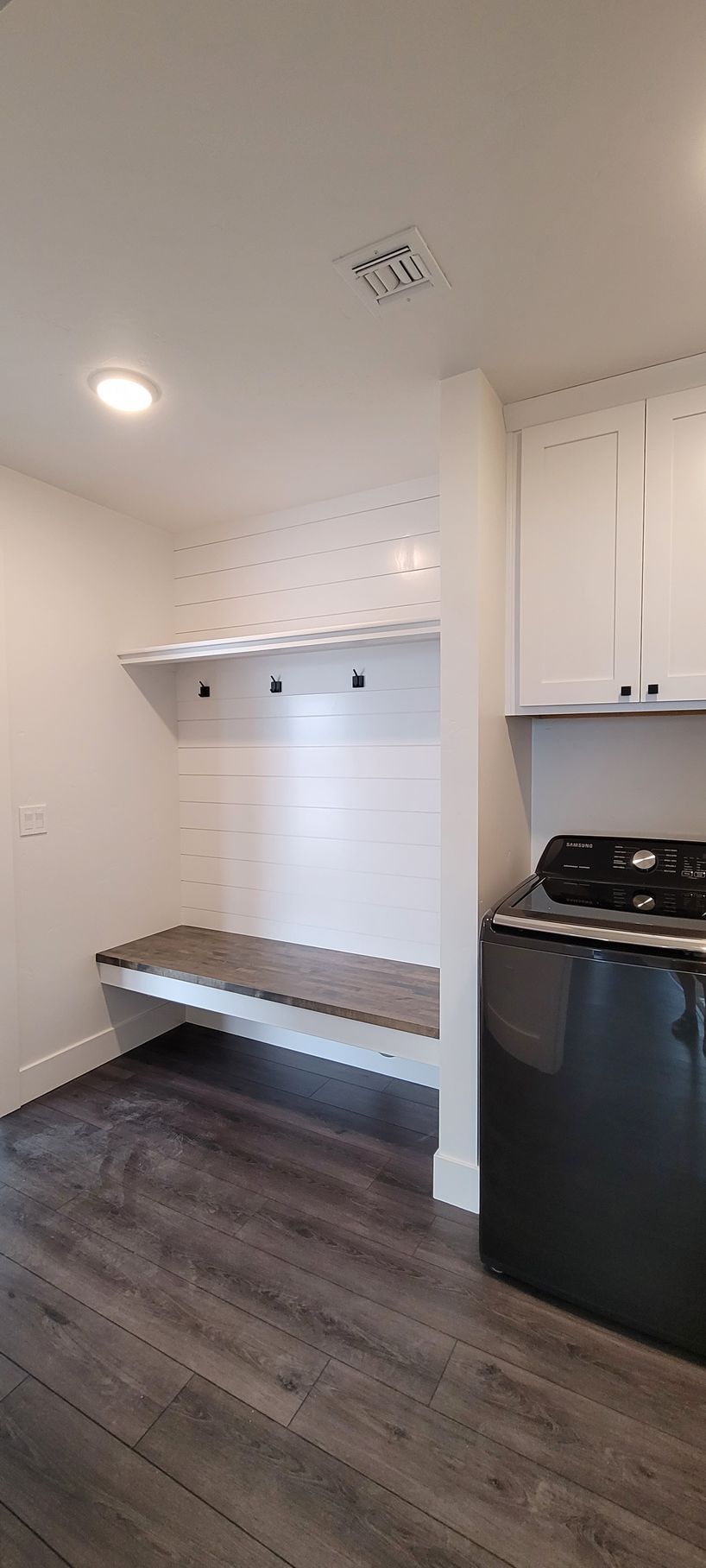 Small kitchen nook with white cabinets, open shelving, black dishwasher, and dark wood floor.