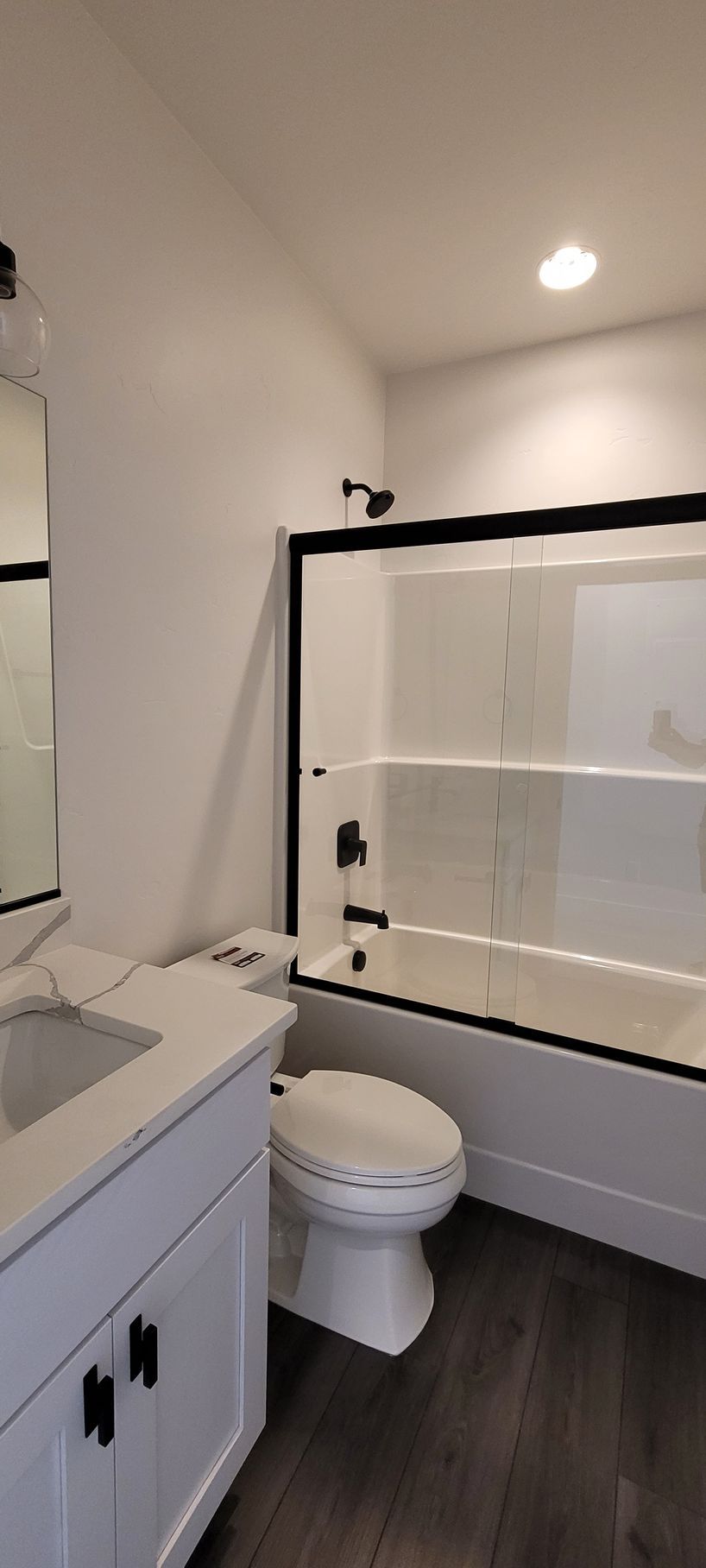 Modern bathroom with white vanity, toilet, black-framed glass shower, and dark wood floor.
